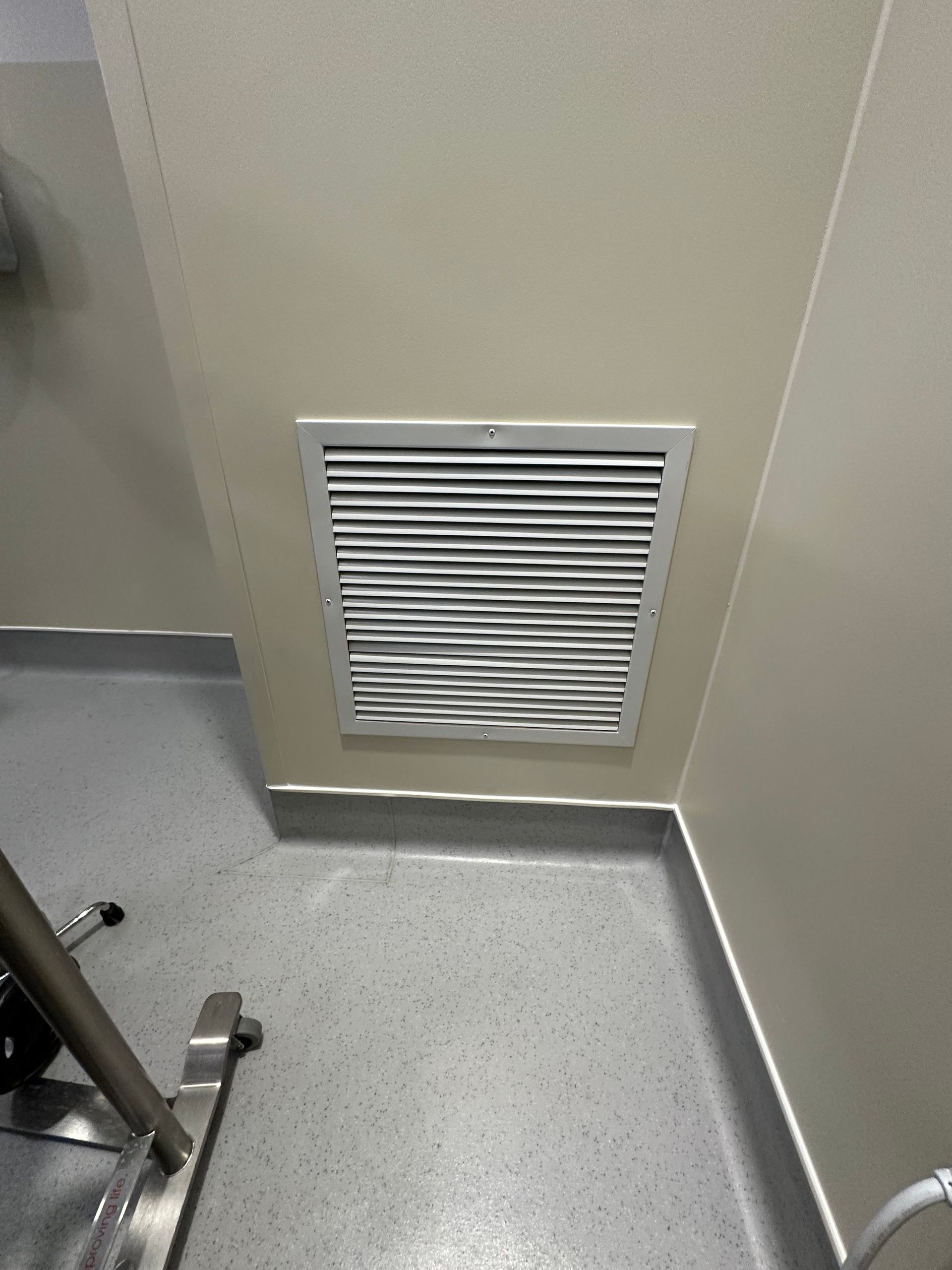 White vent cover in beige wall. Gray-blue floor in corner of room.