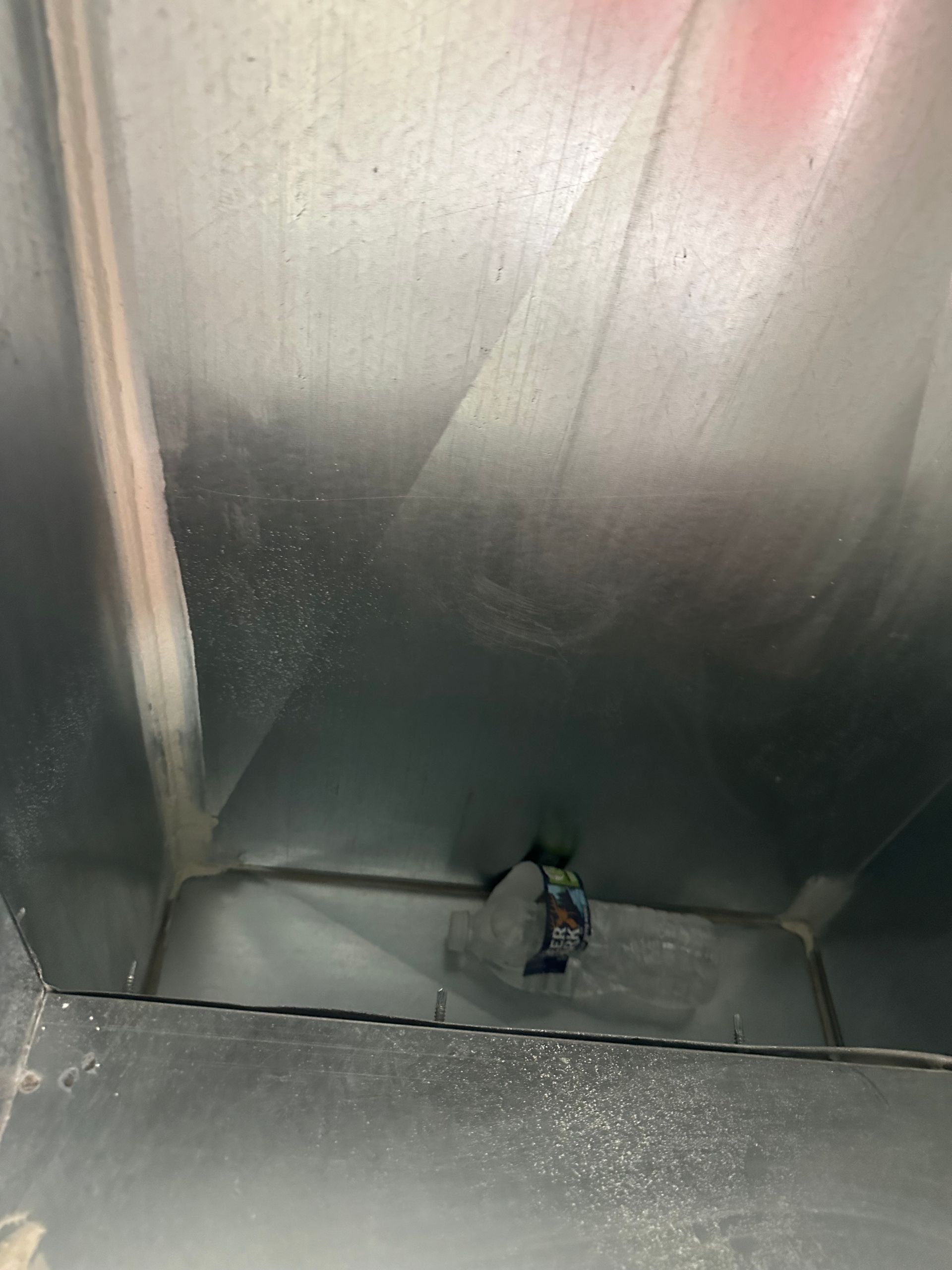 Inside view of a metallic air duct with a small, attached device visible at the bottom.