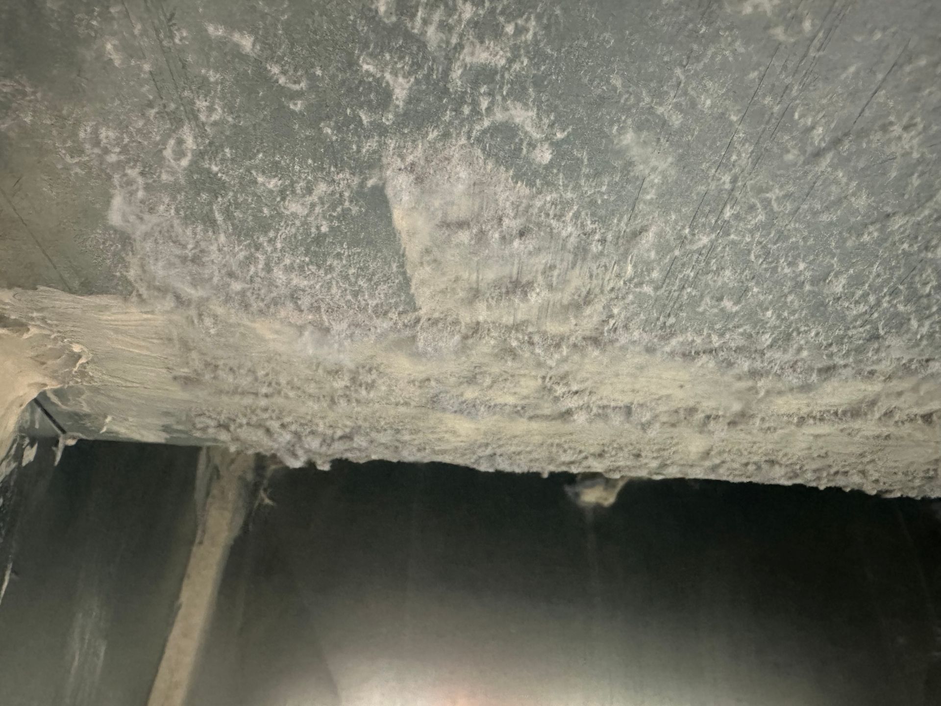 Interior view of a duct with a thick layer of white, flaky substance on its ceiling.