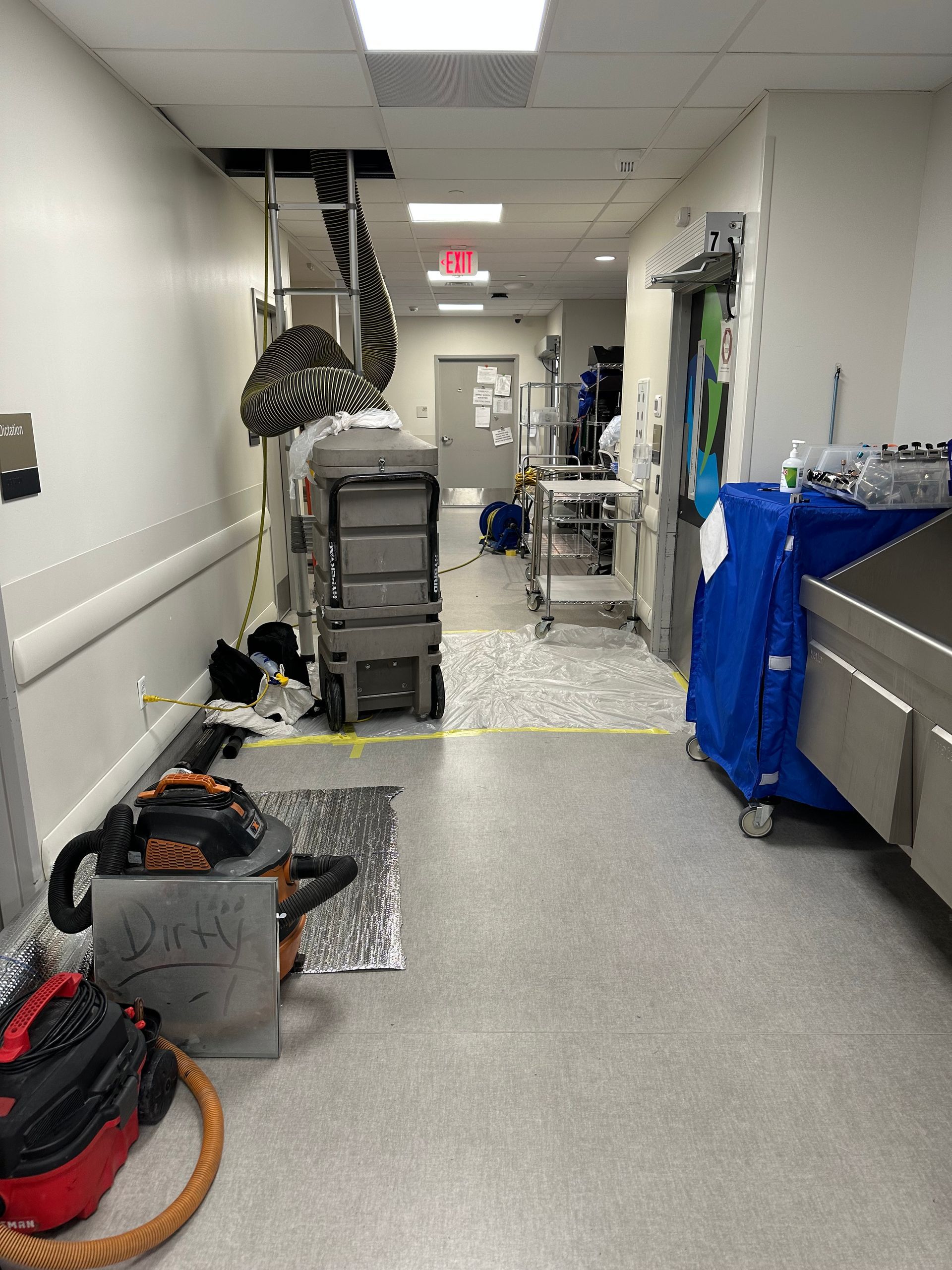 Hospital hallway under construction; equipment, debris, and ceiling access visible.
