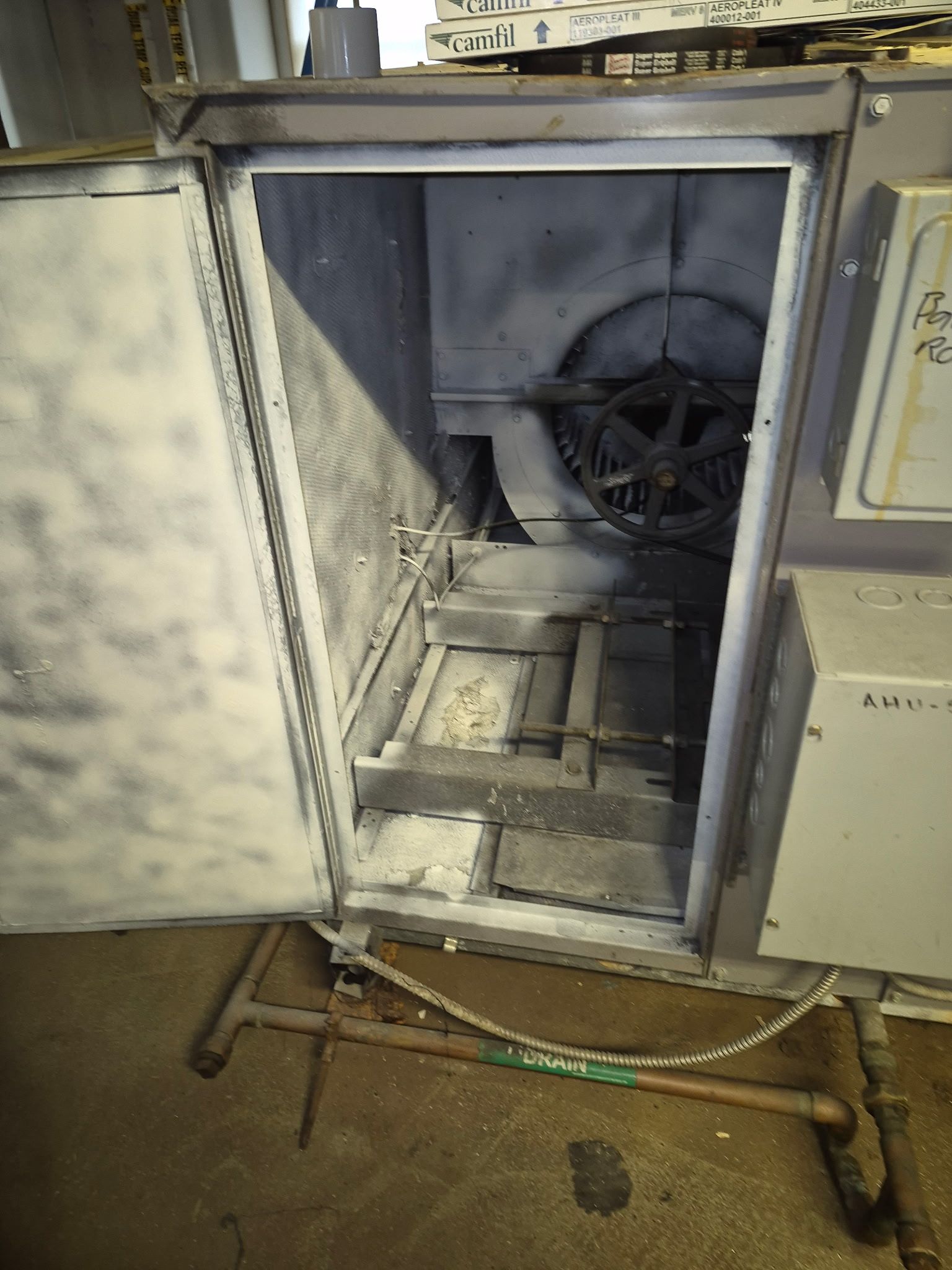 Open industrial machine interior, showing fan and components, with open door. Metal exterior with pipes.