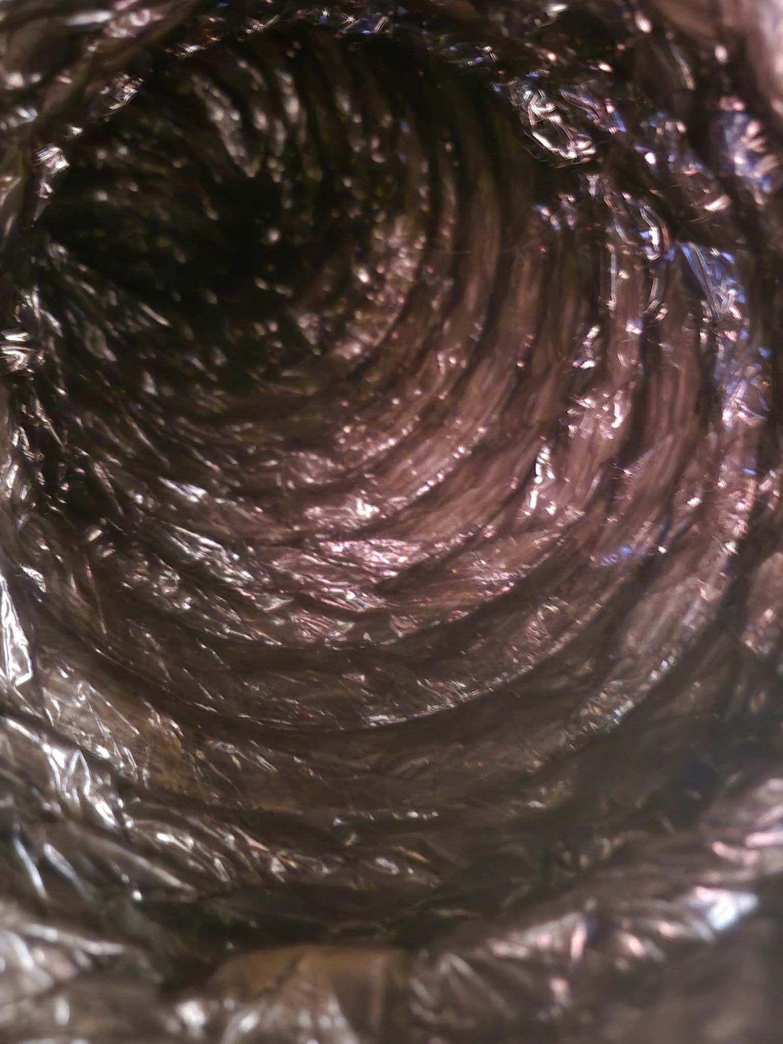 Inside view of a dark, flexible duct with swirling, metallic texture.