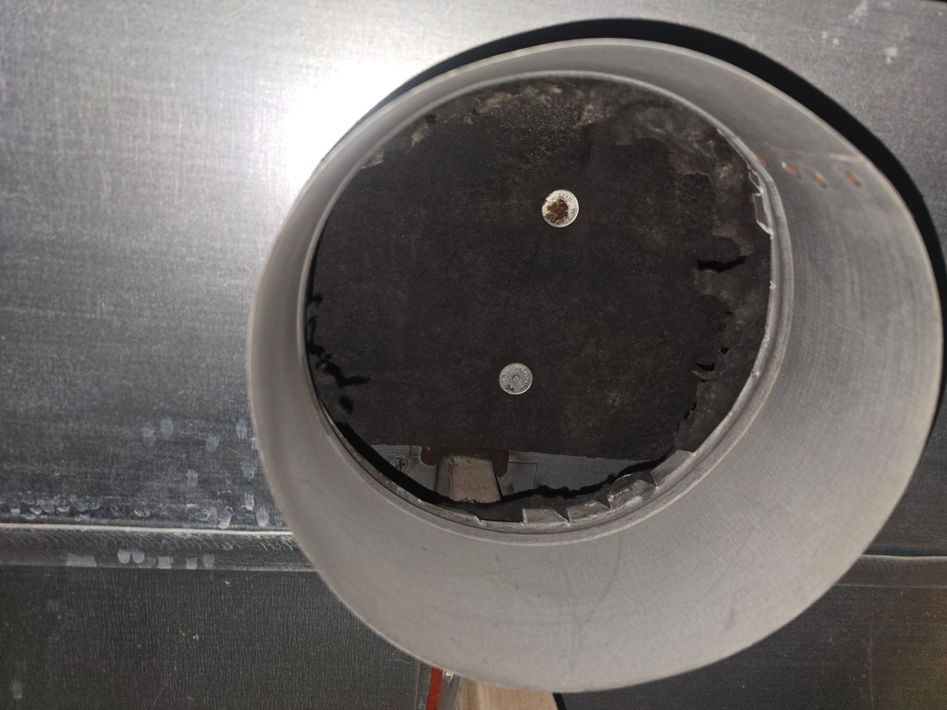 Close-up of a metal pipe's interior. A dark, circular object is inside, with two holes and signs of wear.