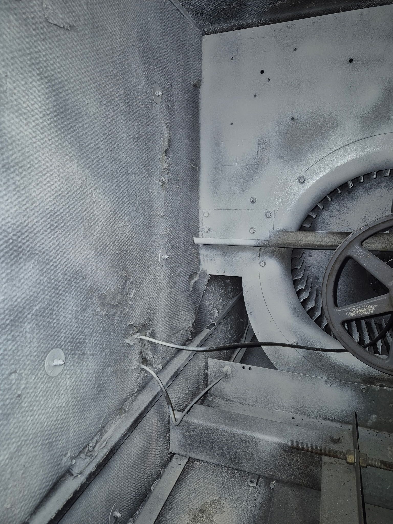 Inside of a dusty industrial structure; a gear and mesh-covered wall.