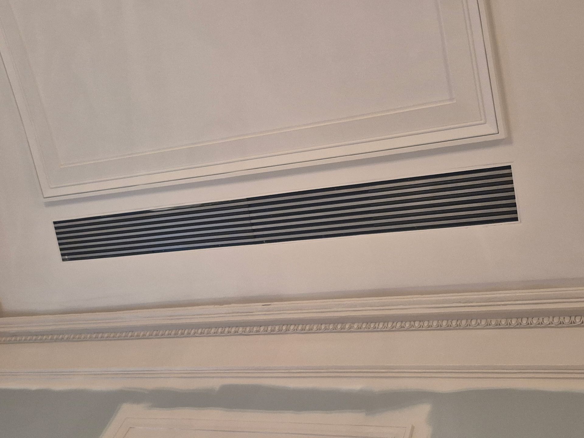 Ceiling with rectangular air vent and ornate molding.