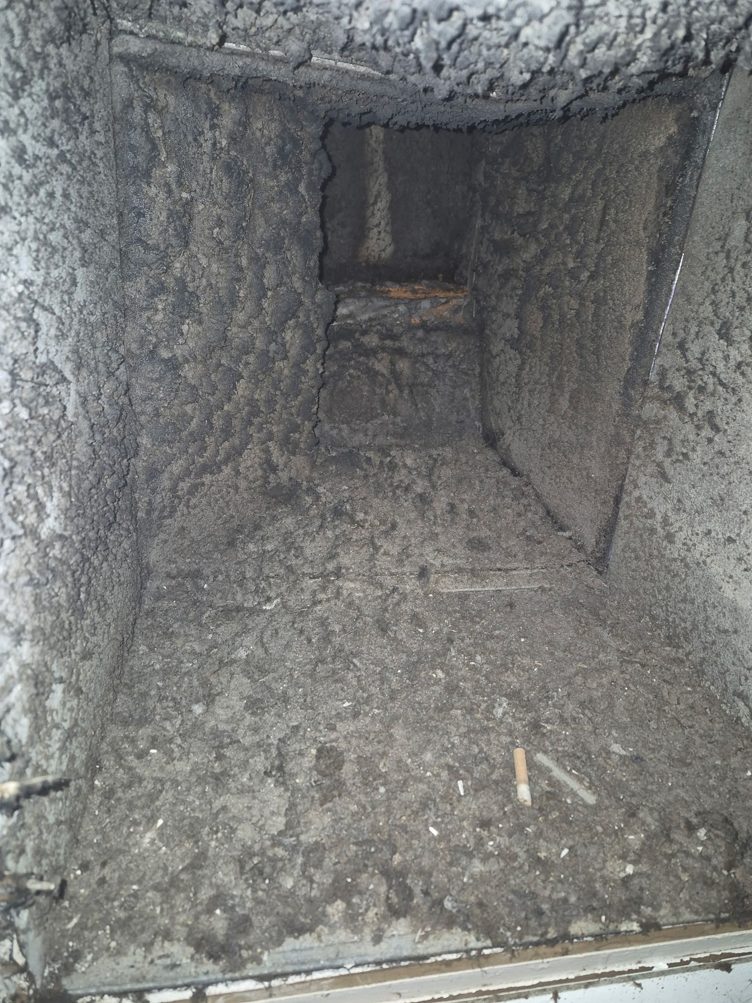 Interior view of a heavily soiled air vent, coated in thick layers of black debris.