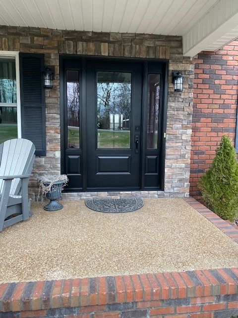 Front porch with black door, brick exterior, potted plants, and gray deck chair