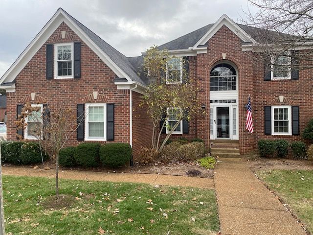 brick house with trees, bushes and flag on right side of stone steps