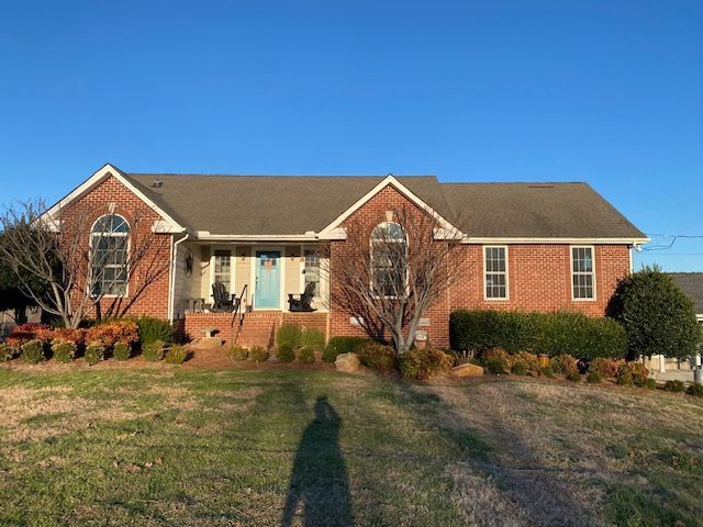 Red brick house with trees and bushes. Blue front door, stone steps