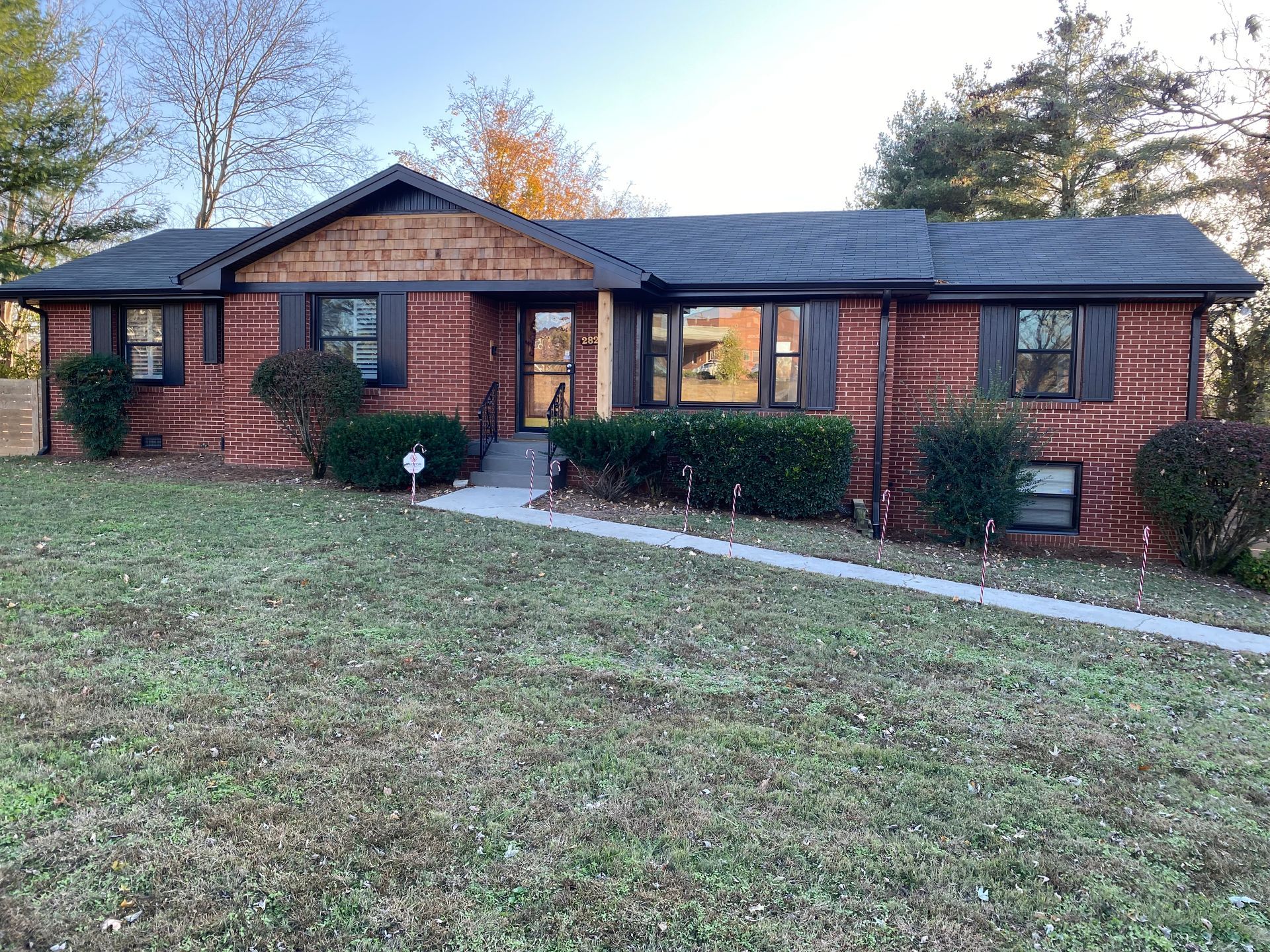 Brick ranch-style house with dark trim and a brown front porch. Green bushes and a sidewalk lead to the front door.