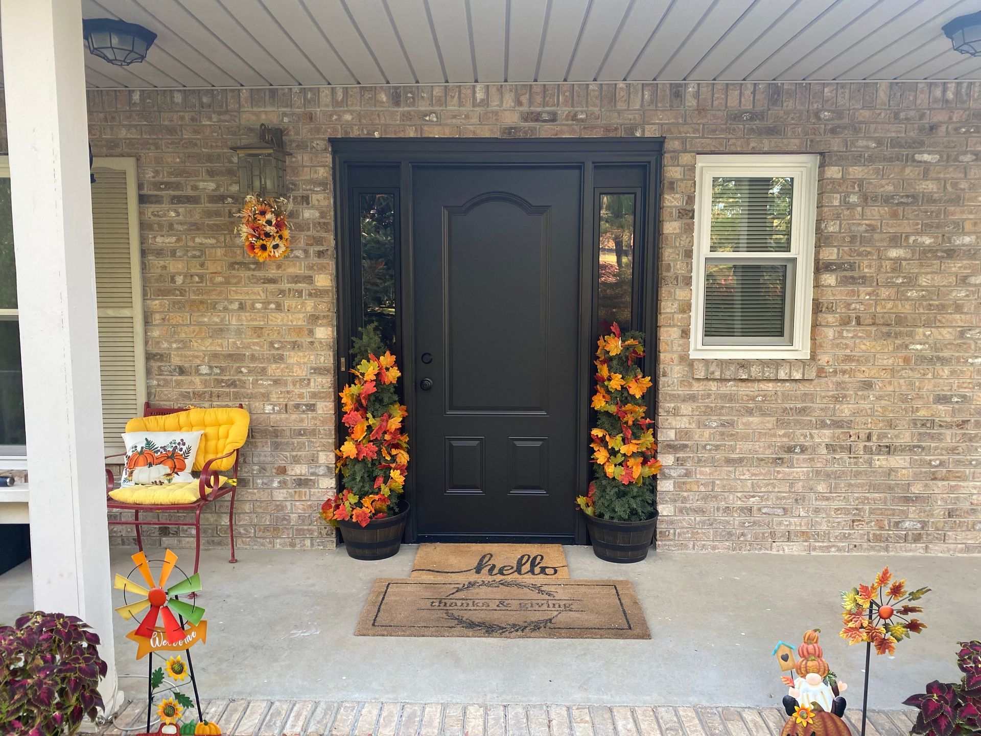 Front porch with black door, autumn decorations, brick exterior, potted plants, and 