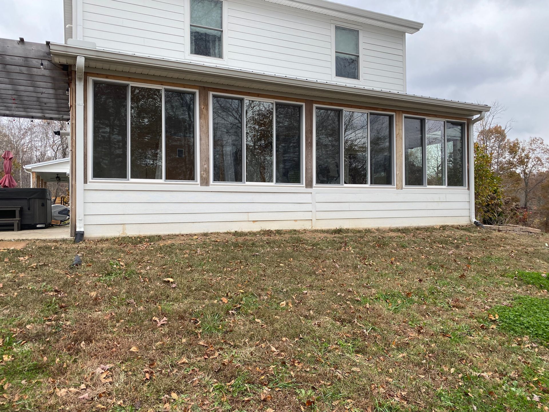 White two-story house with a sunroom, situated on a lawn with scattered brown leaves.