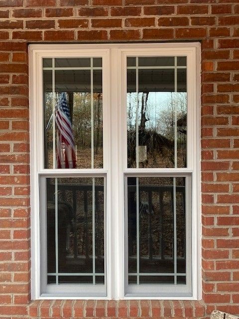 Two white-framed windows set in a red brick wall. An American flag hangs inside the left window.