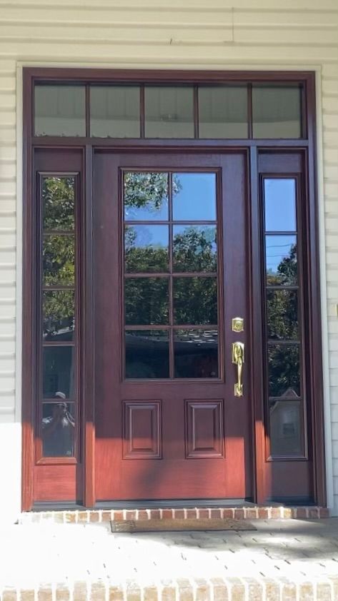 Red wooden front door with sidelights and transom windows; gold hardware, brick steps.