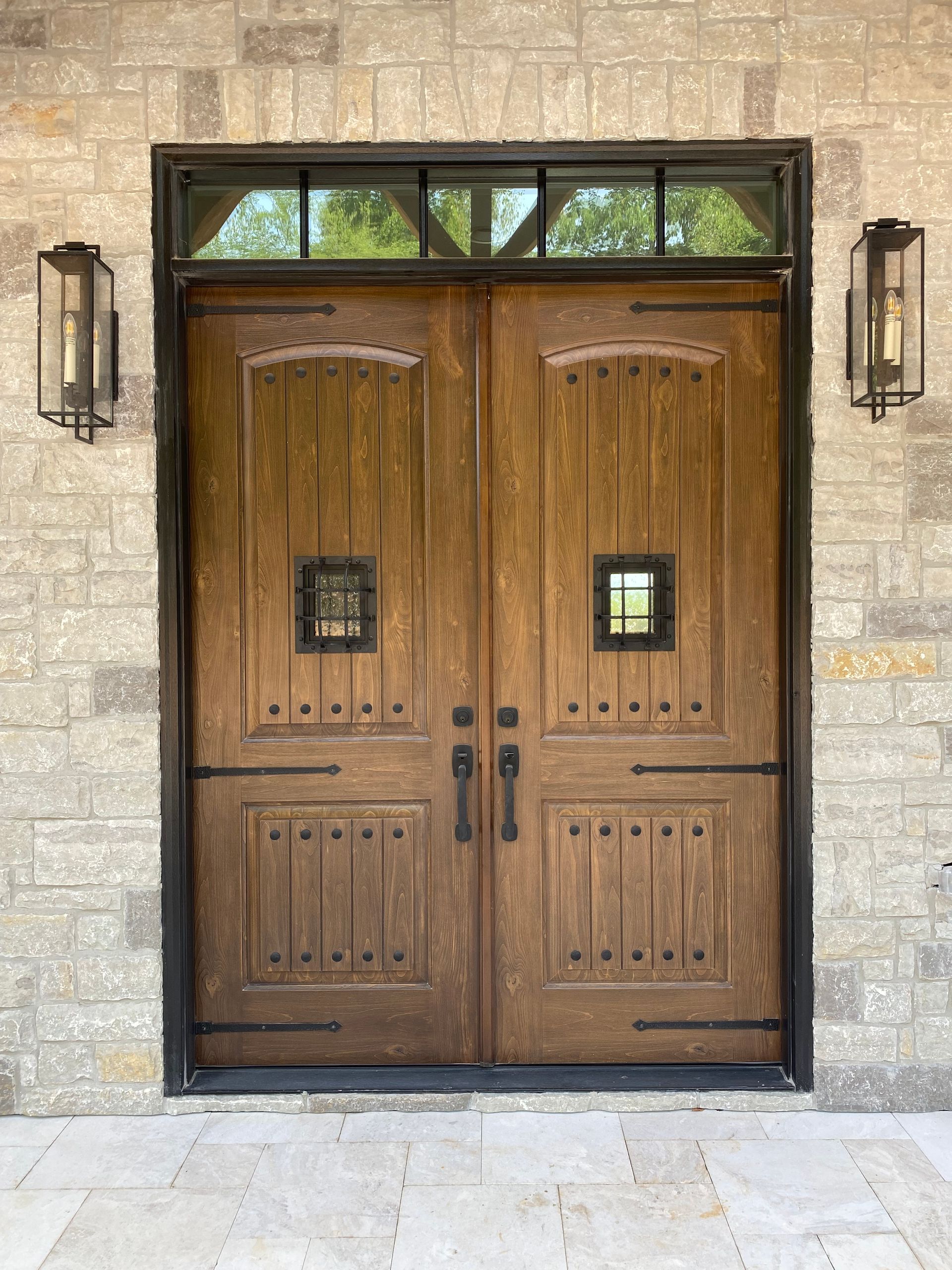 Wooden double doors with sidelights and sconces set into a stone wall.