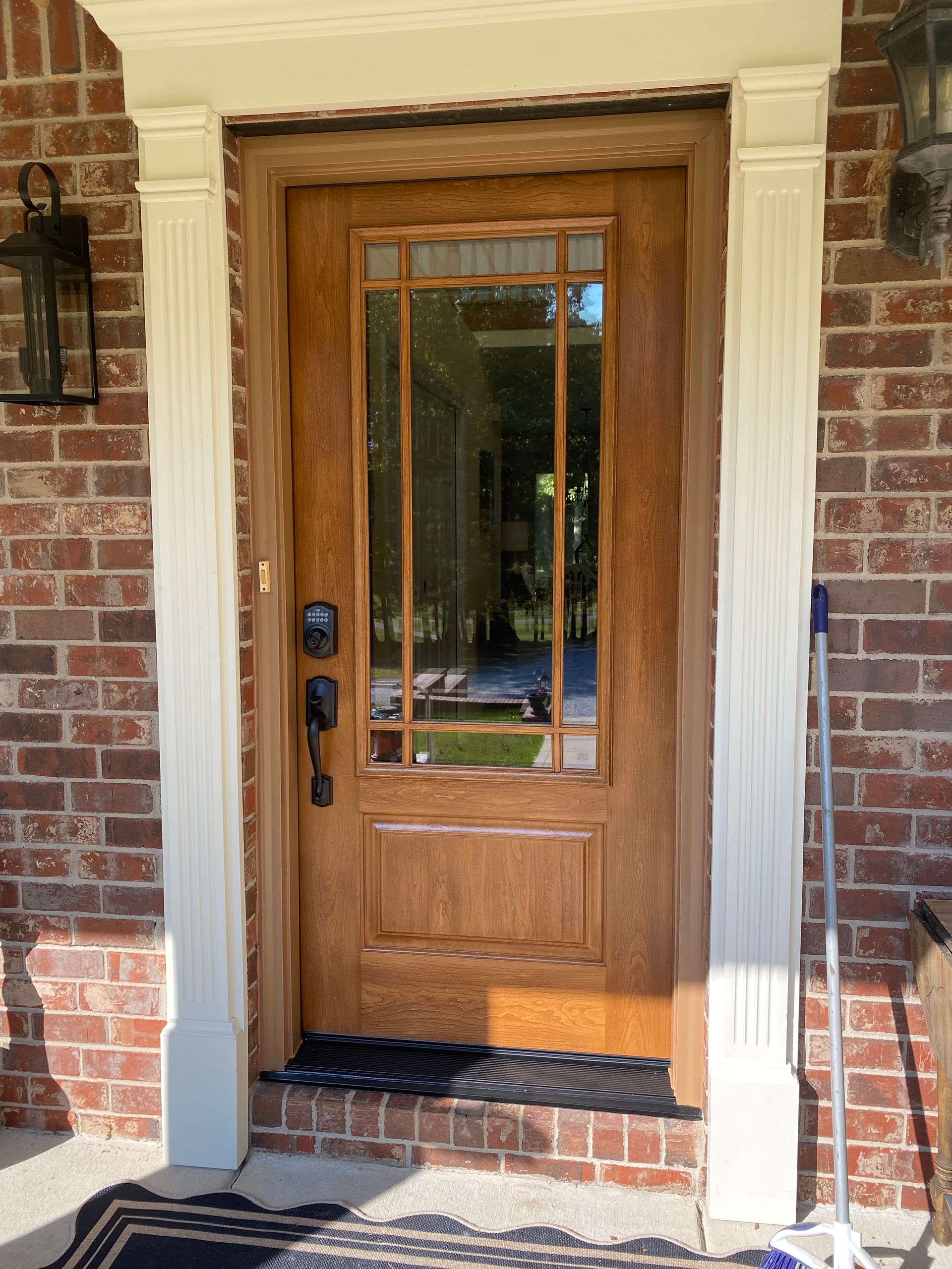 Wooden front door with glass panels and sidelights, set in a brick wall with white trim.