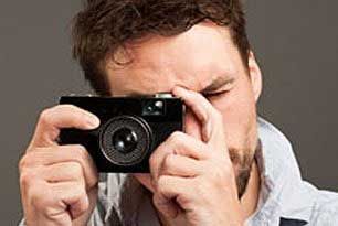 Man holding a black camera, taking a photo, indoors.