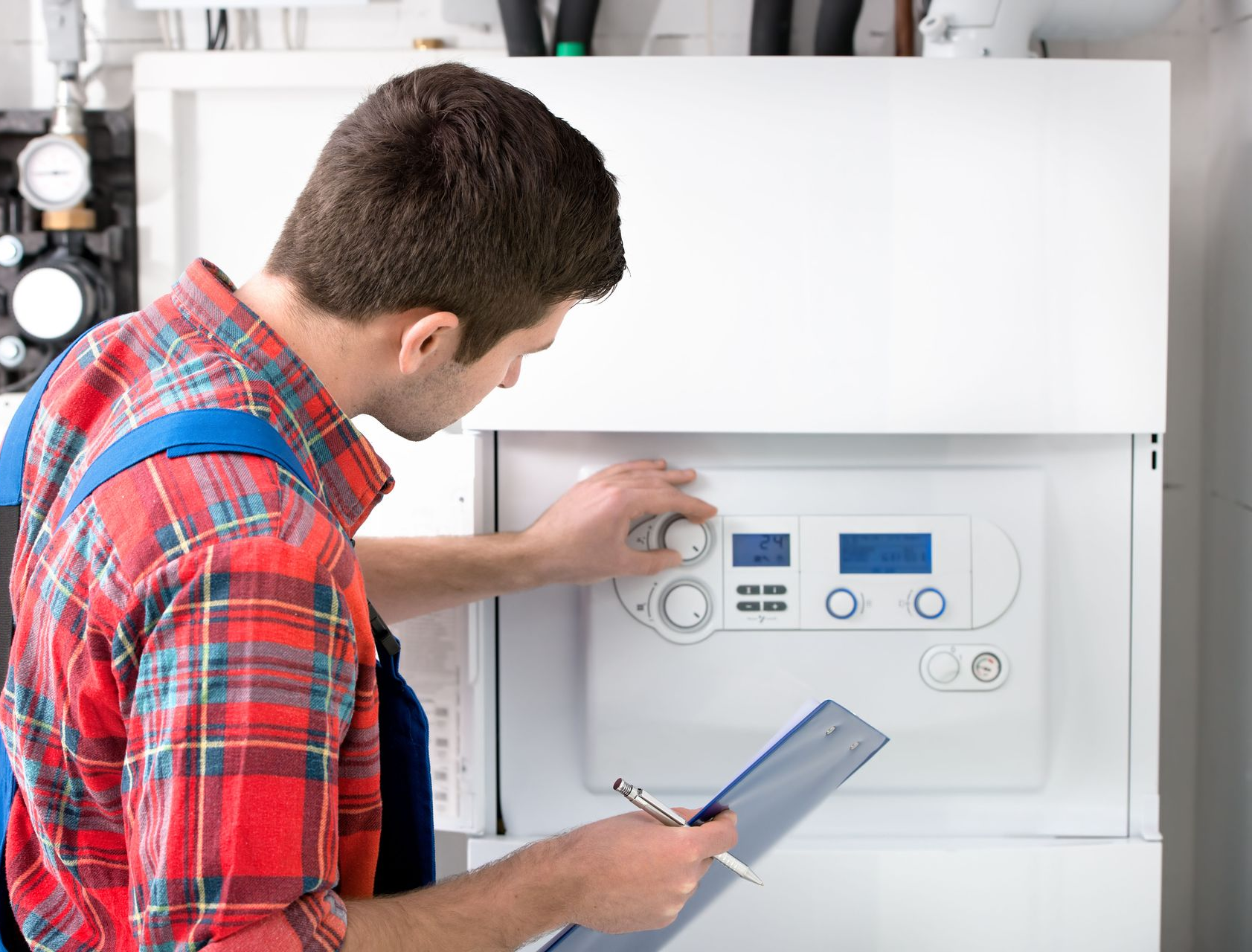 Person in red plaid shirt adjusting a white heating unit with a clipboard.