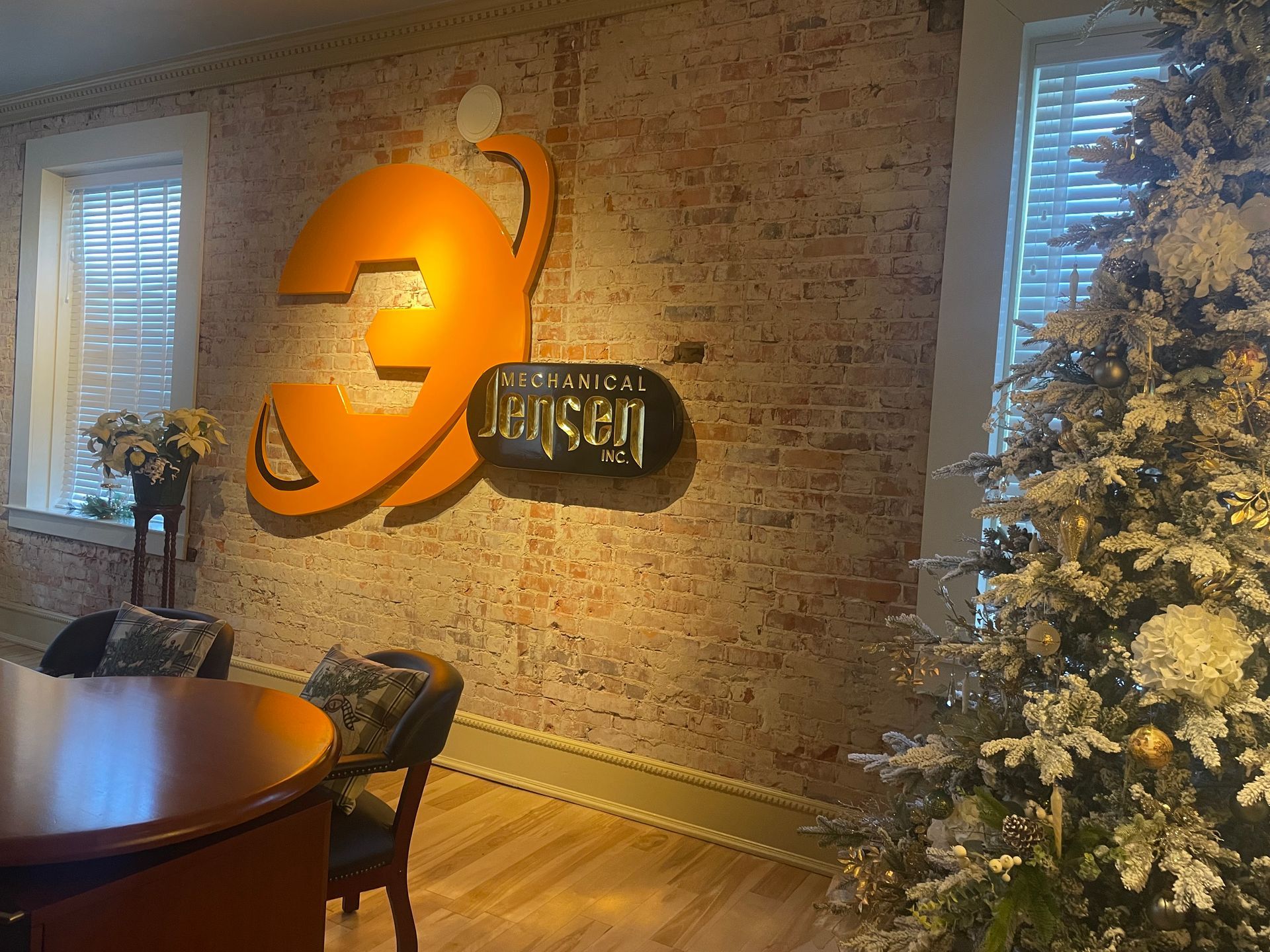 Brick wall with a large orange logo. A Christmas tree is on the right, and a round table on the left.