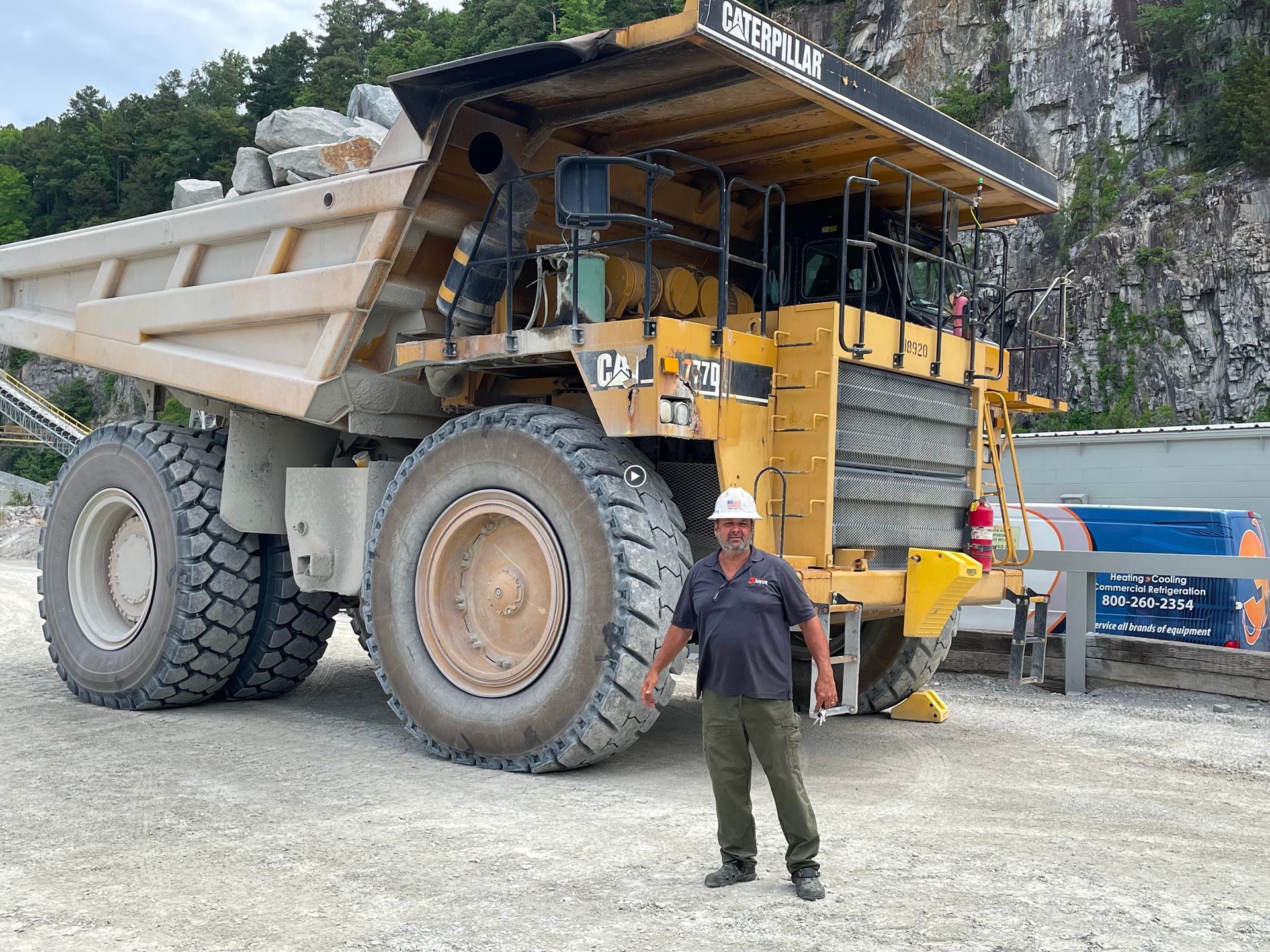 Man stands next to a massive yellow Caterpillar mining truck in a quarry.
