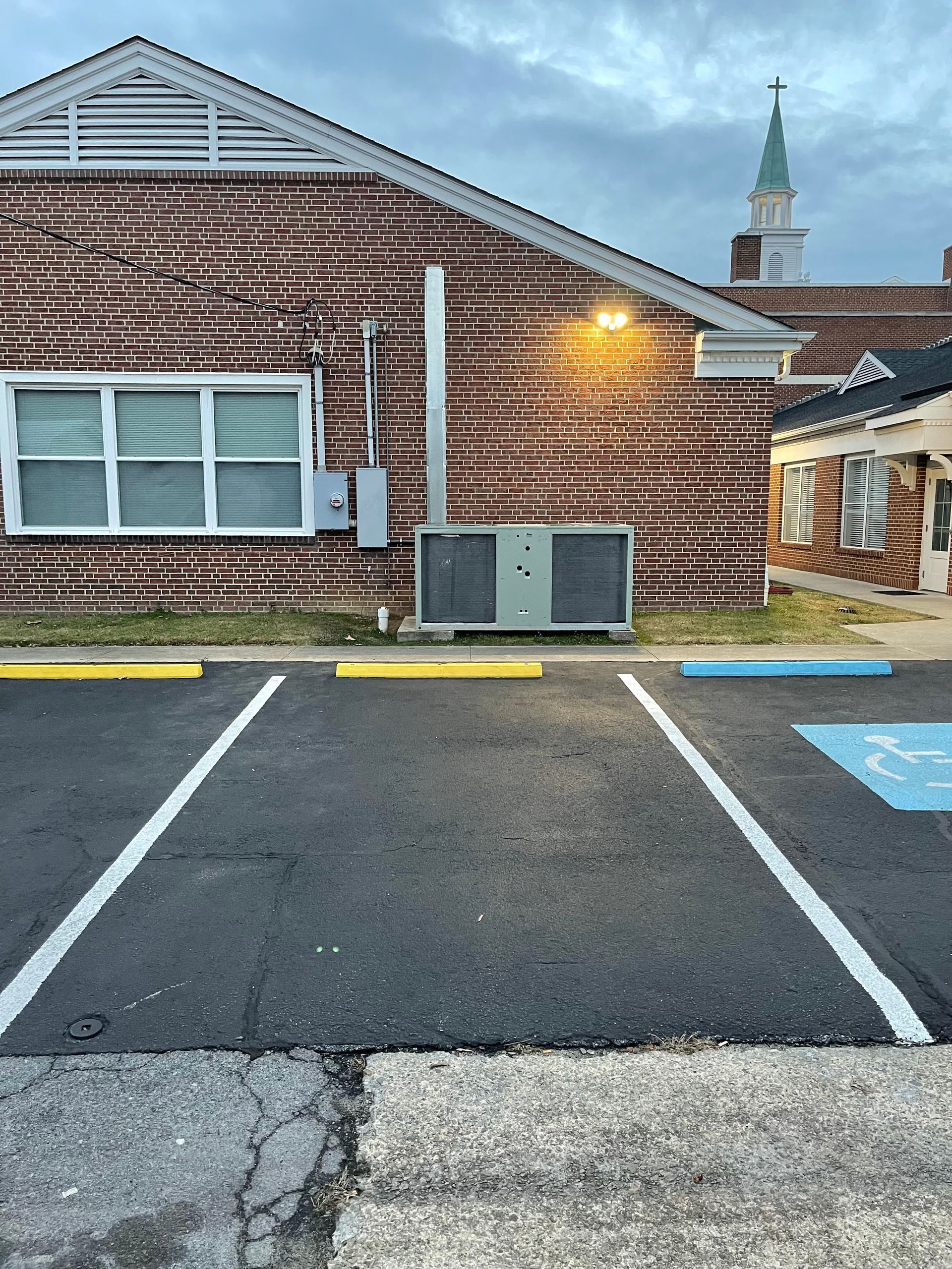 Brick building exterior with parking spaces, an AC unit, and a steeple in the background.