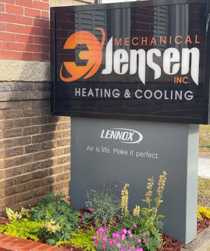 Sign for Jensen Mechanical Inc. with Lennox ad, set in front of brick building and garden.