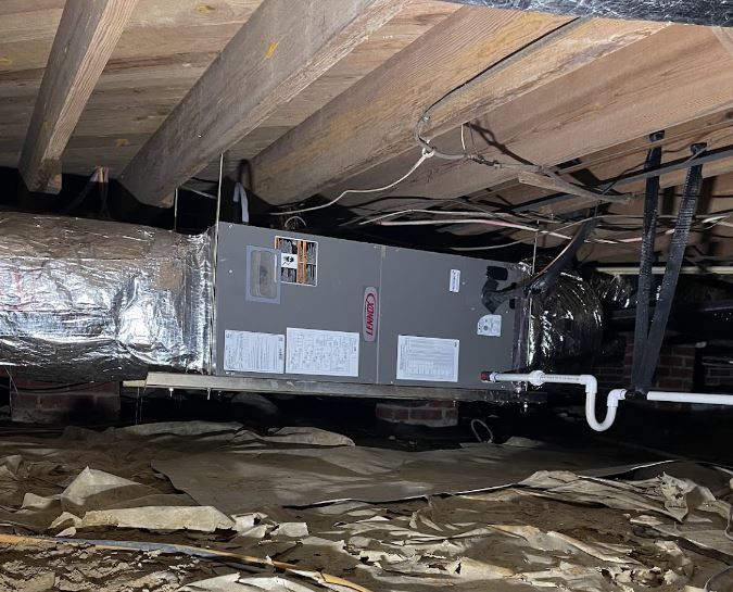 HVAC unit installed in a crawl space under a wooden structure; foil-wrapped ductwork visible.