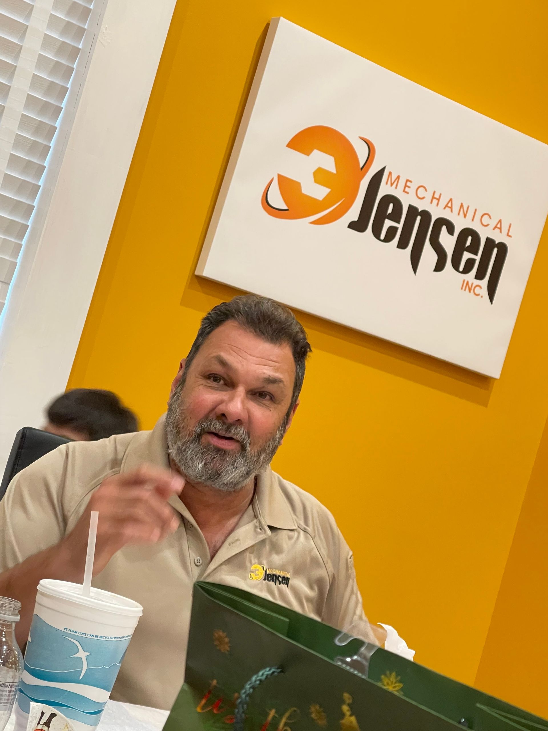 Man with beard seated, pointing, in front of 