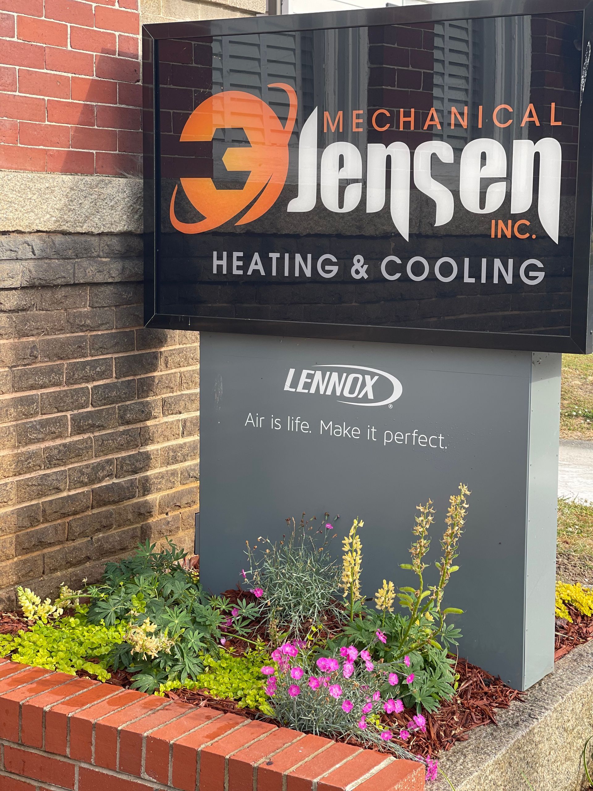 Sign for Jensen Mechanical Inc. Heating & Cooling; Lennox sign below, small garden in front.