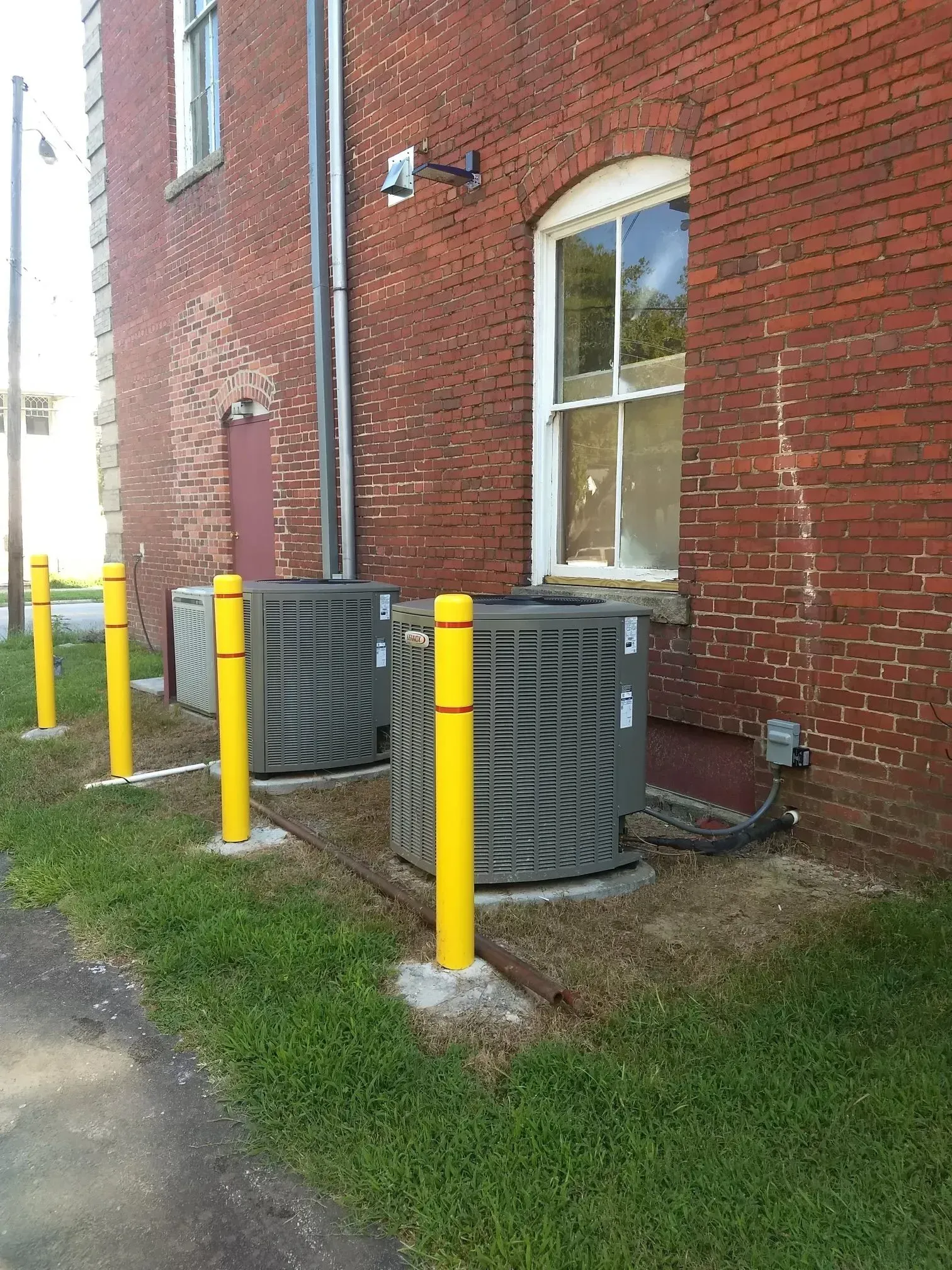 Brick building with two air conditioning units protected by yellow posts.