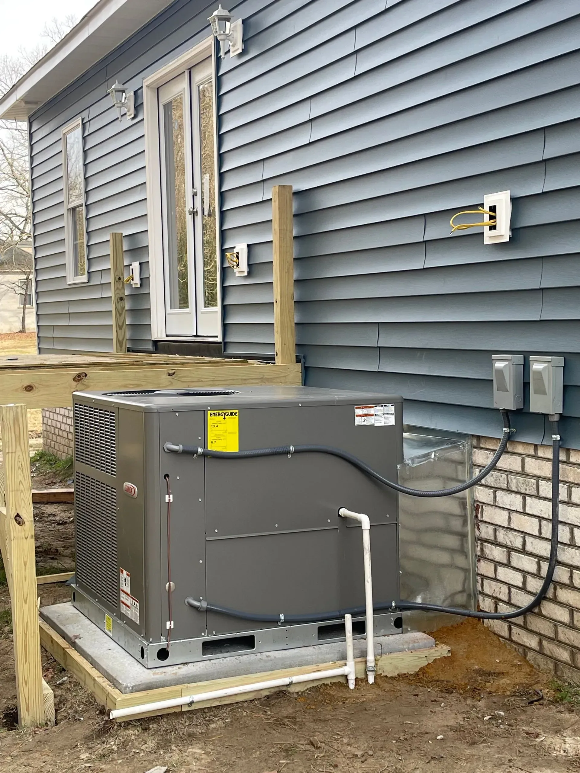 Exterior view of a gray HVAC unit on a concrete pad next to a blue house with a wooden deck.