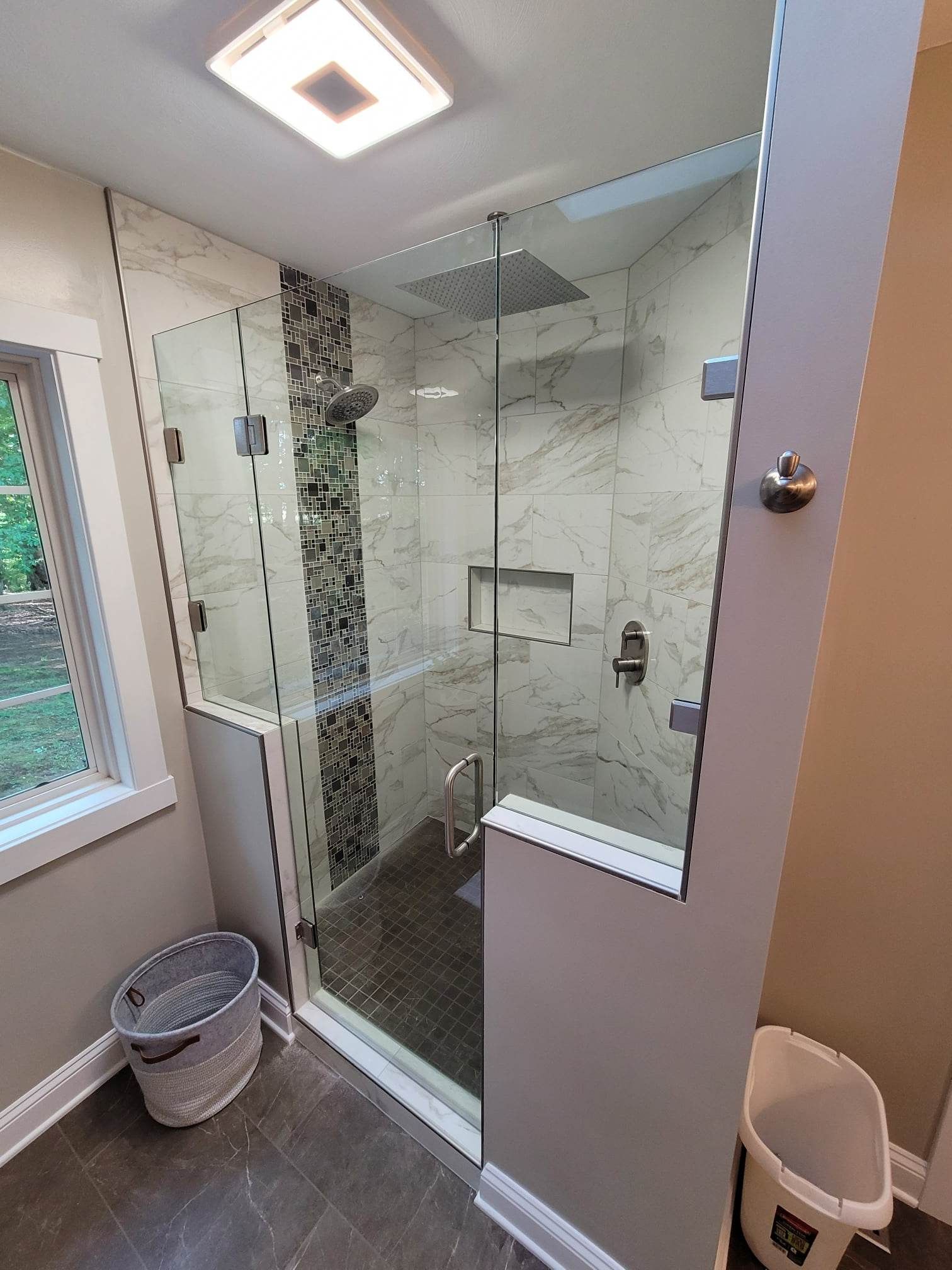A bathroom with a glass shower door and a window.
