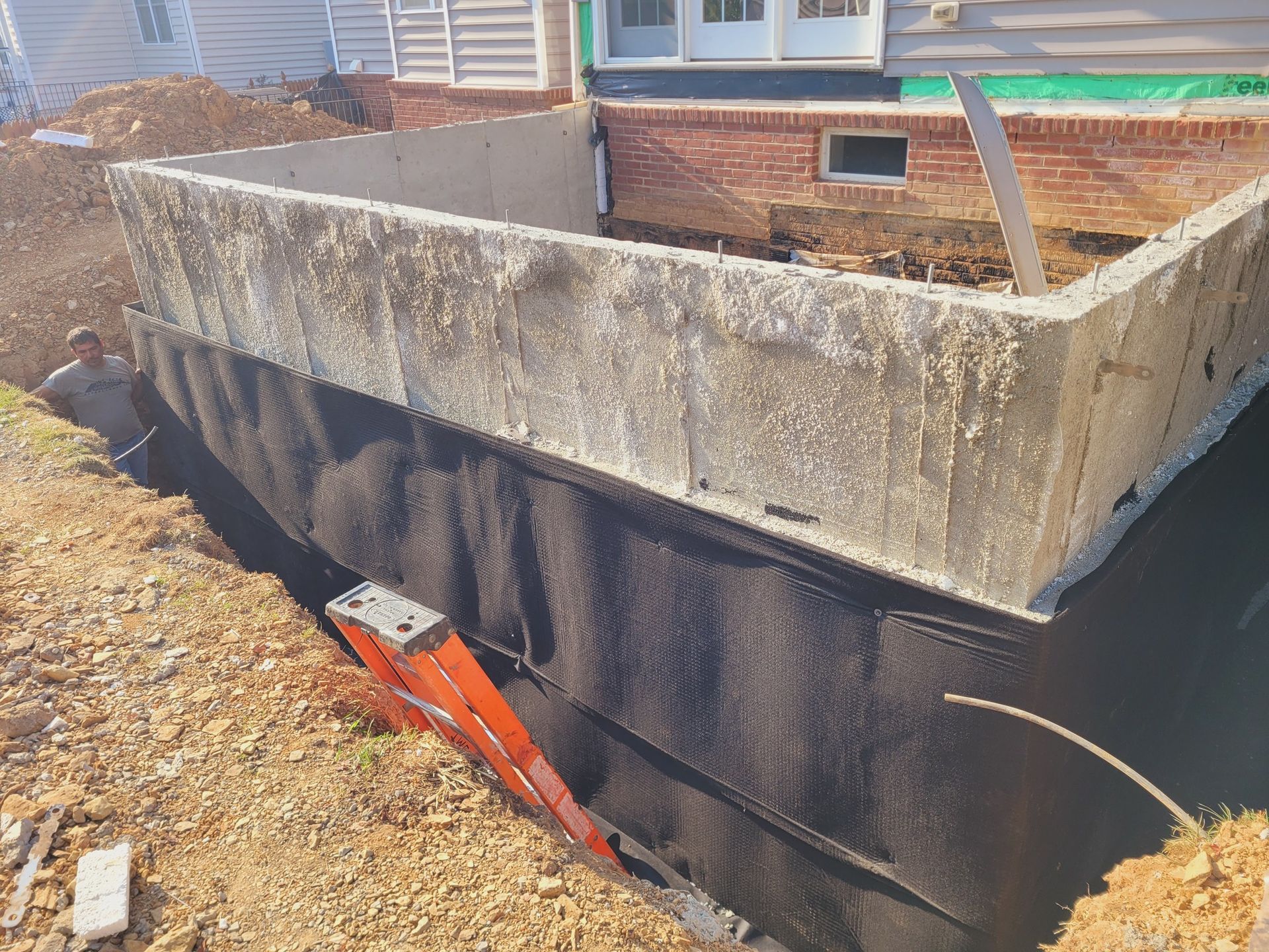 A ladder is sitting in the dirt next to a concrete wall.
