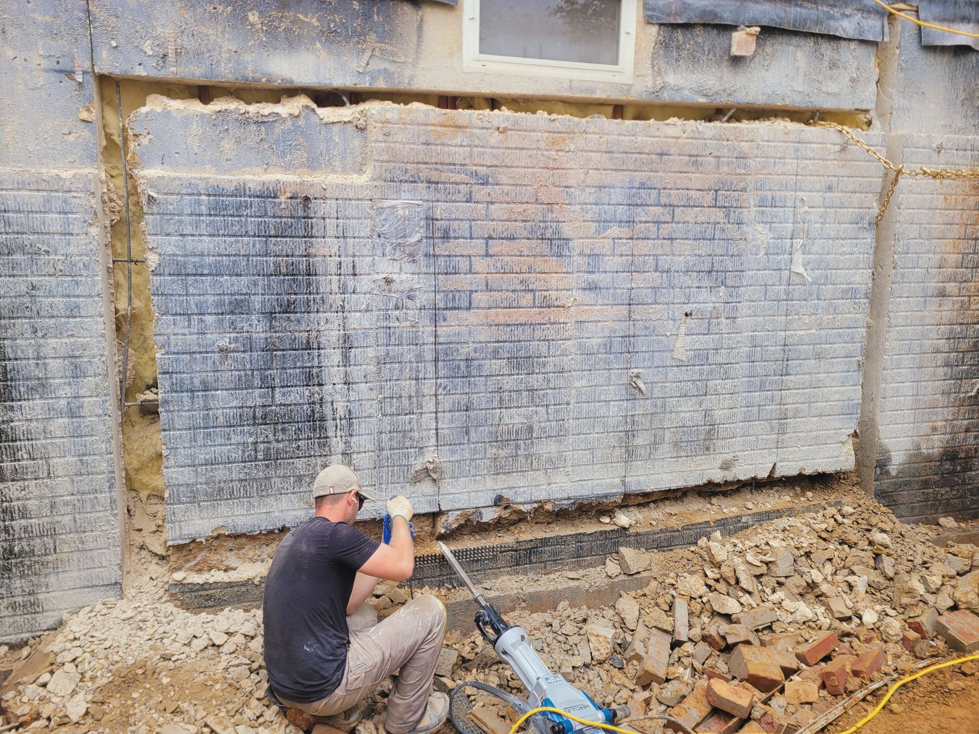 A man is kneeling down in front of a brick wall.