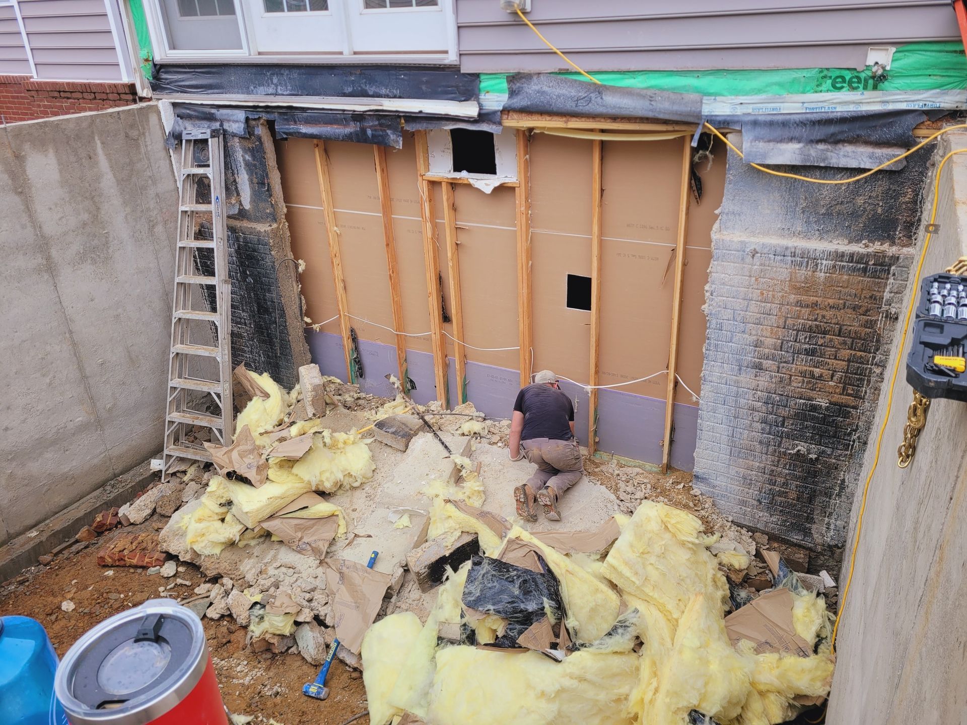 A man is kneeling in front of a wall that is being remodeled.