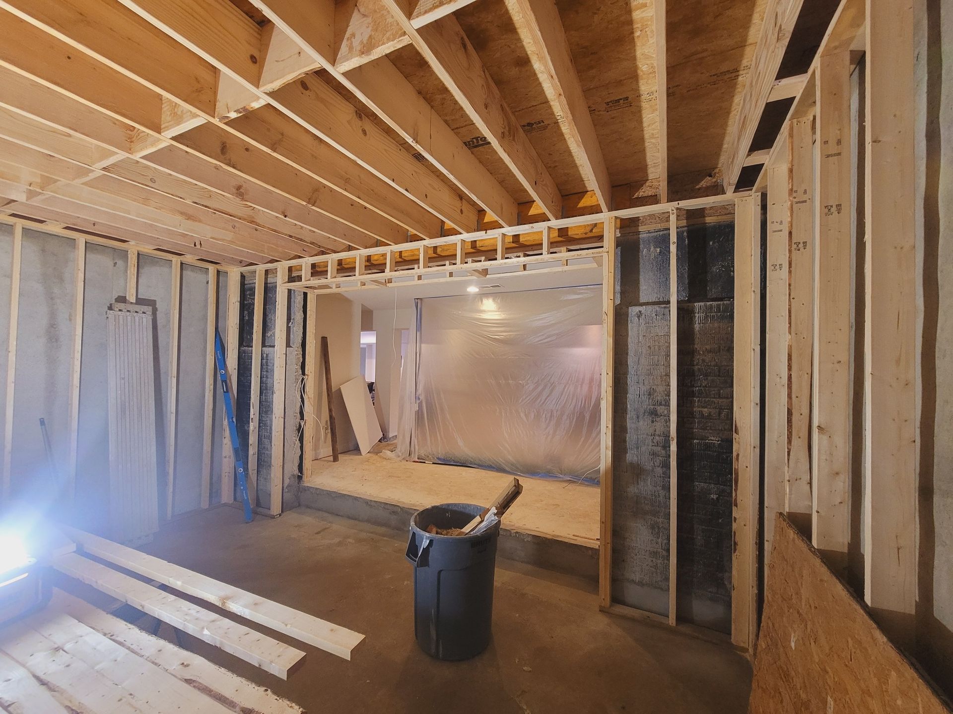 A room under construction with a black trash can in the middle