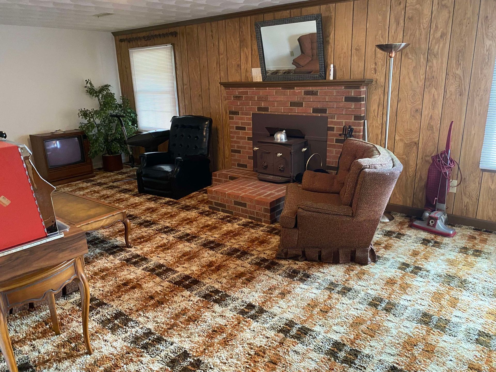 A living room with a fireplace, chairs, a piano, and a vacuum cleaner.