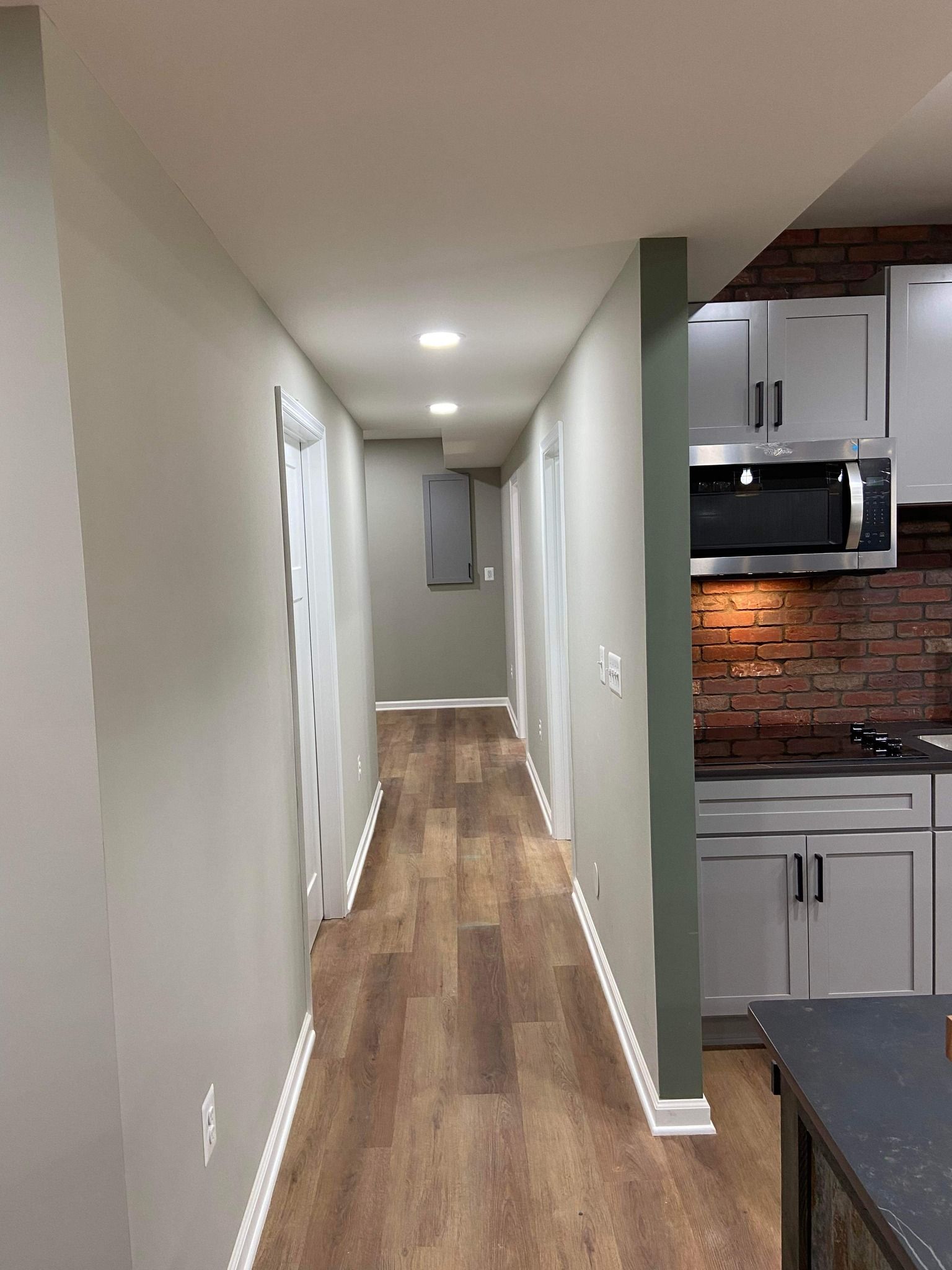 A long hallway leading to a kitchen with hardwood floors and white cabinets.