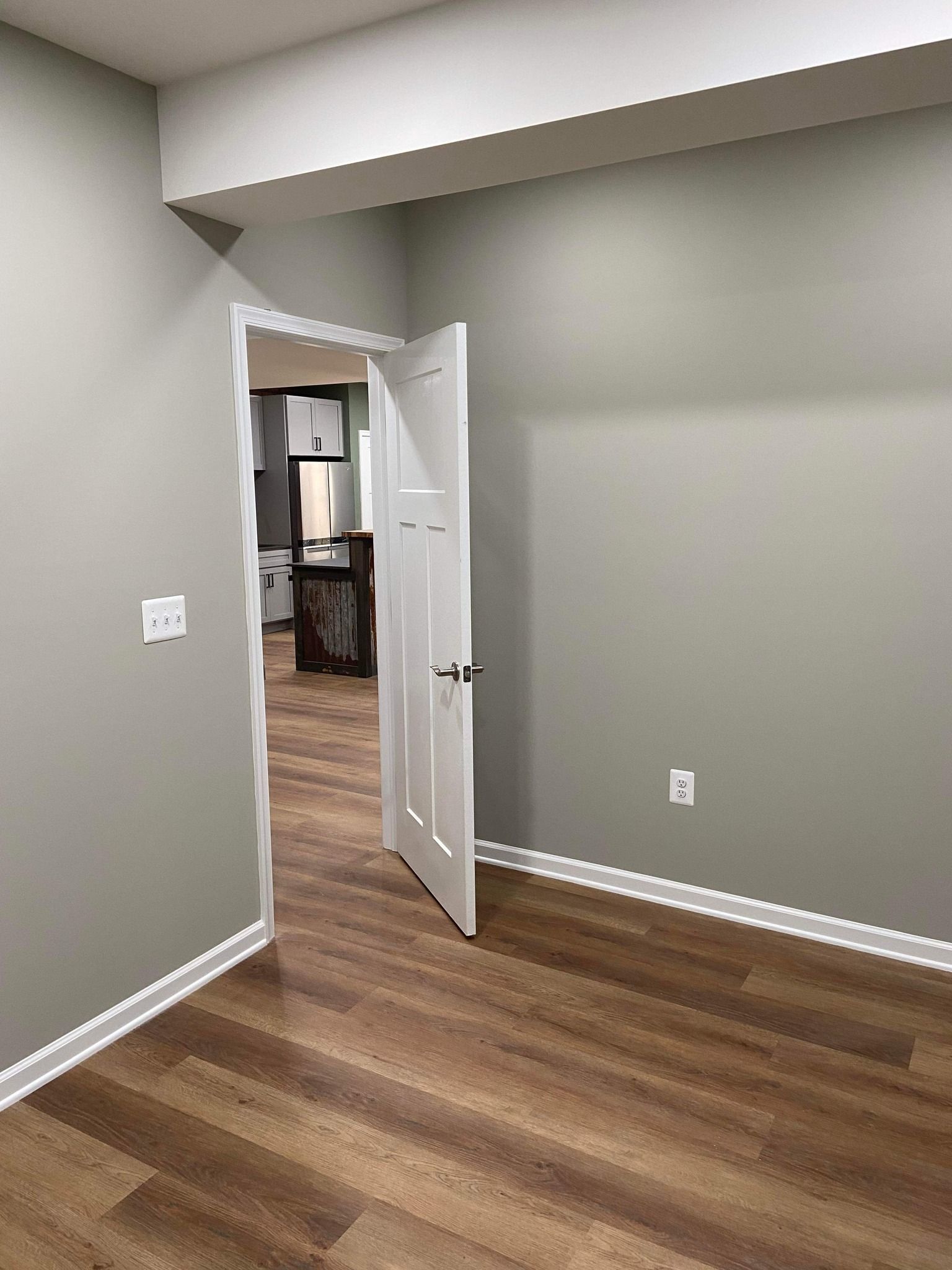An empty room with hardwood floors and a door open leading to a kitchen.