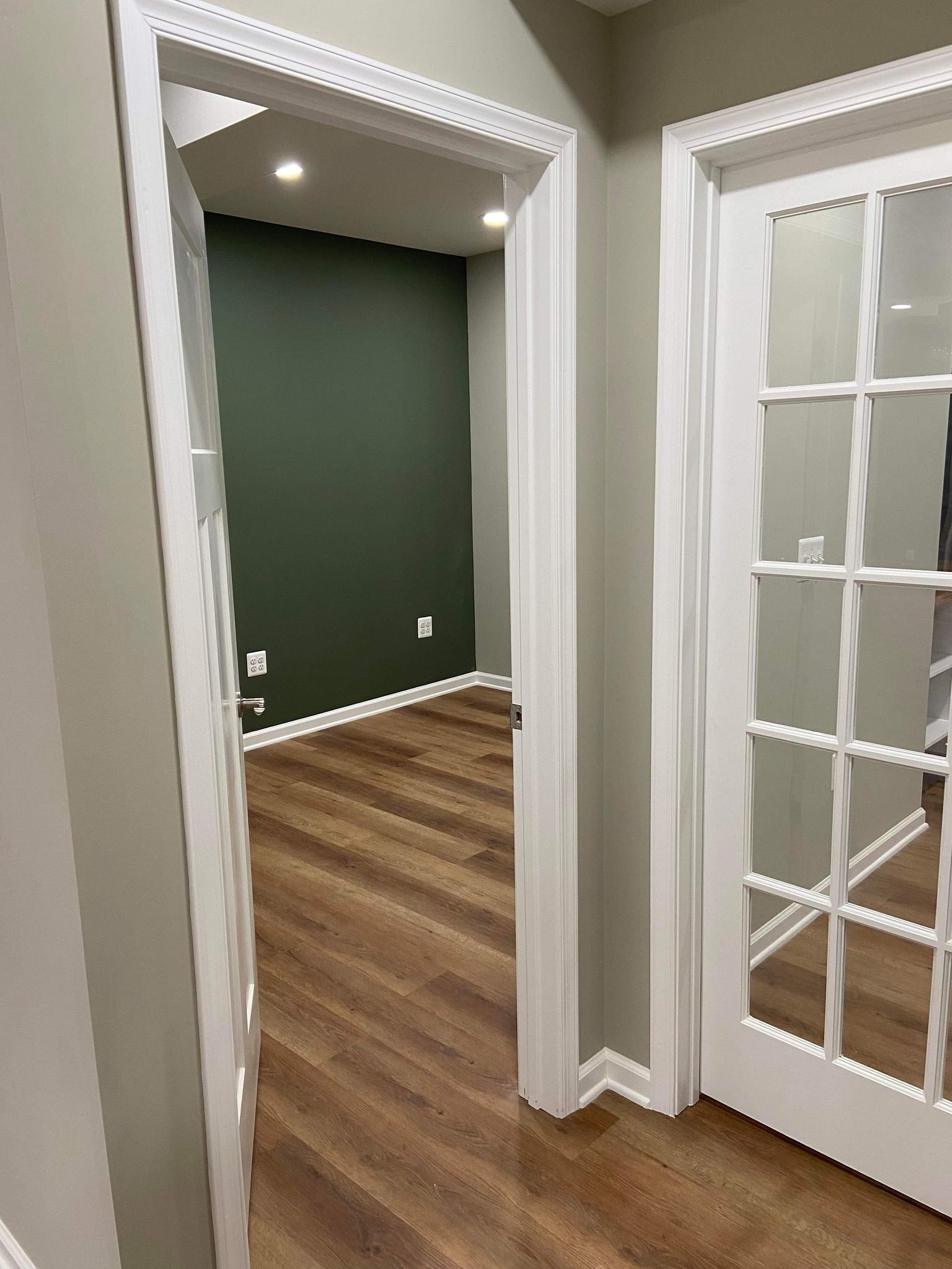A hallway with hardwood floors and french doors leading to a room.