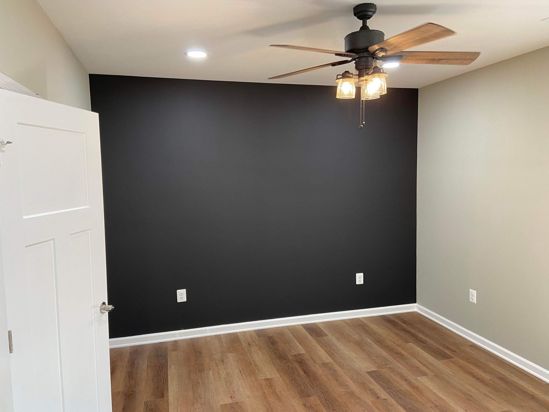 A bedroom with a black wall and a ceiling fan.