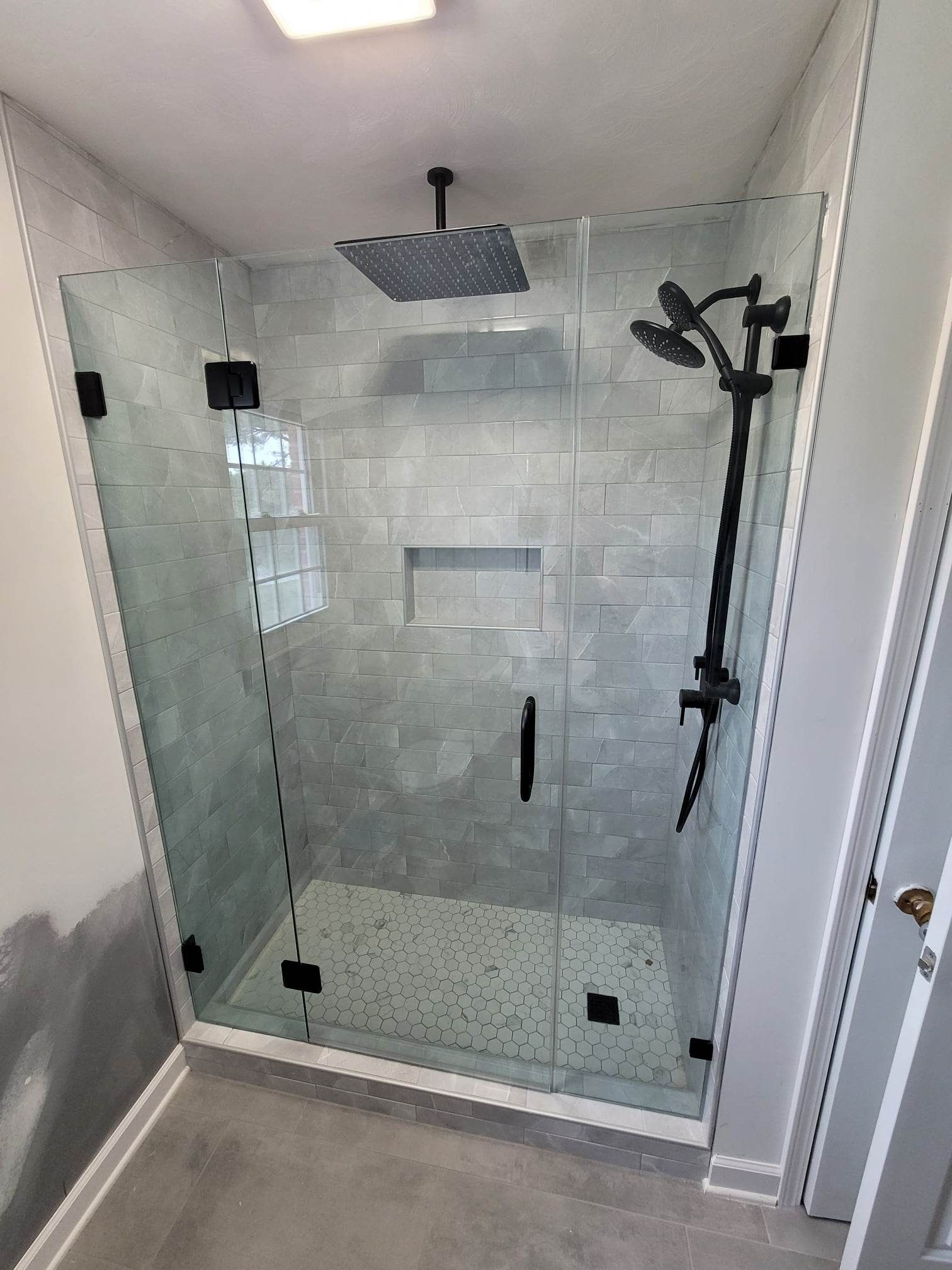 A bathroom with a walk in shower with a glass door and a black shower head.