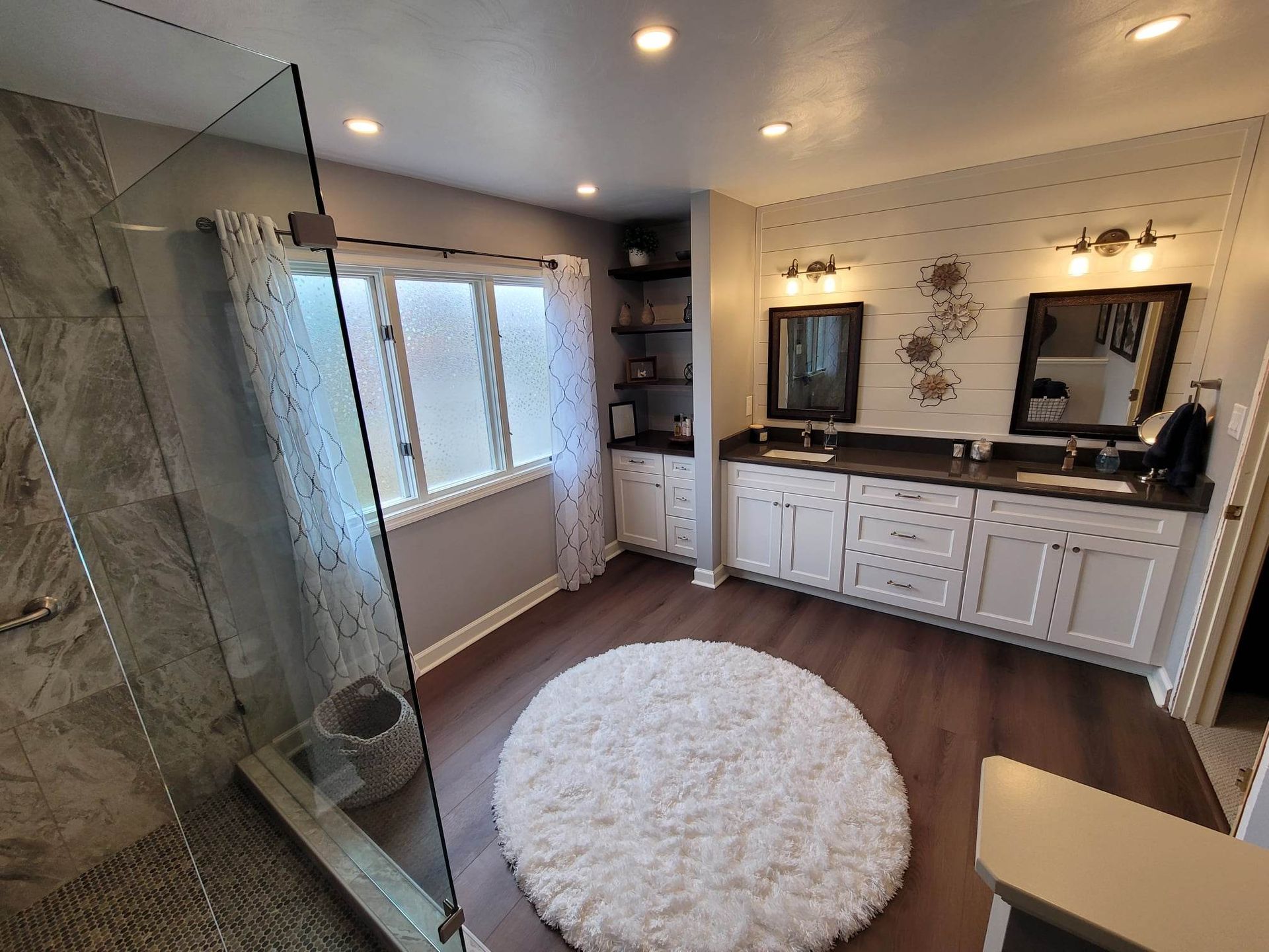 A bathroom with a walk in shower , sinks , mirrors and a rug.