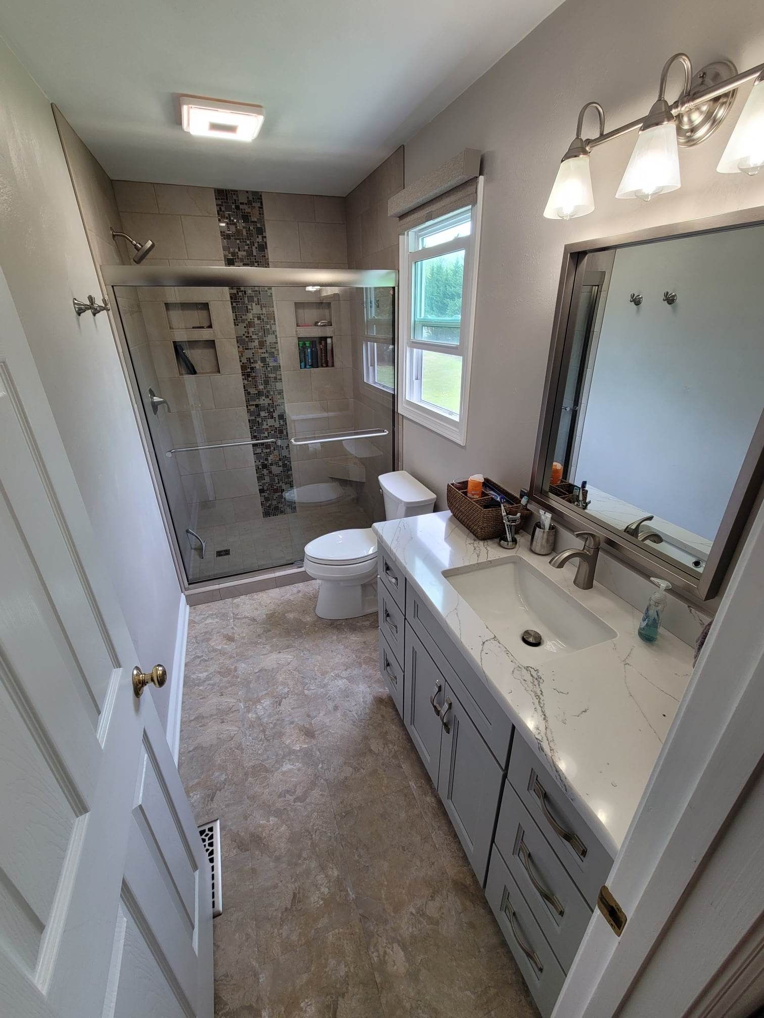 A bathroom with a sink , toilet , shower and mirror.