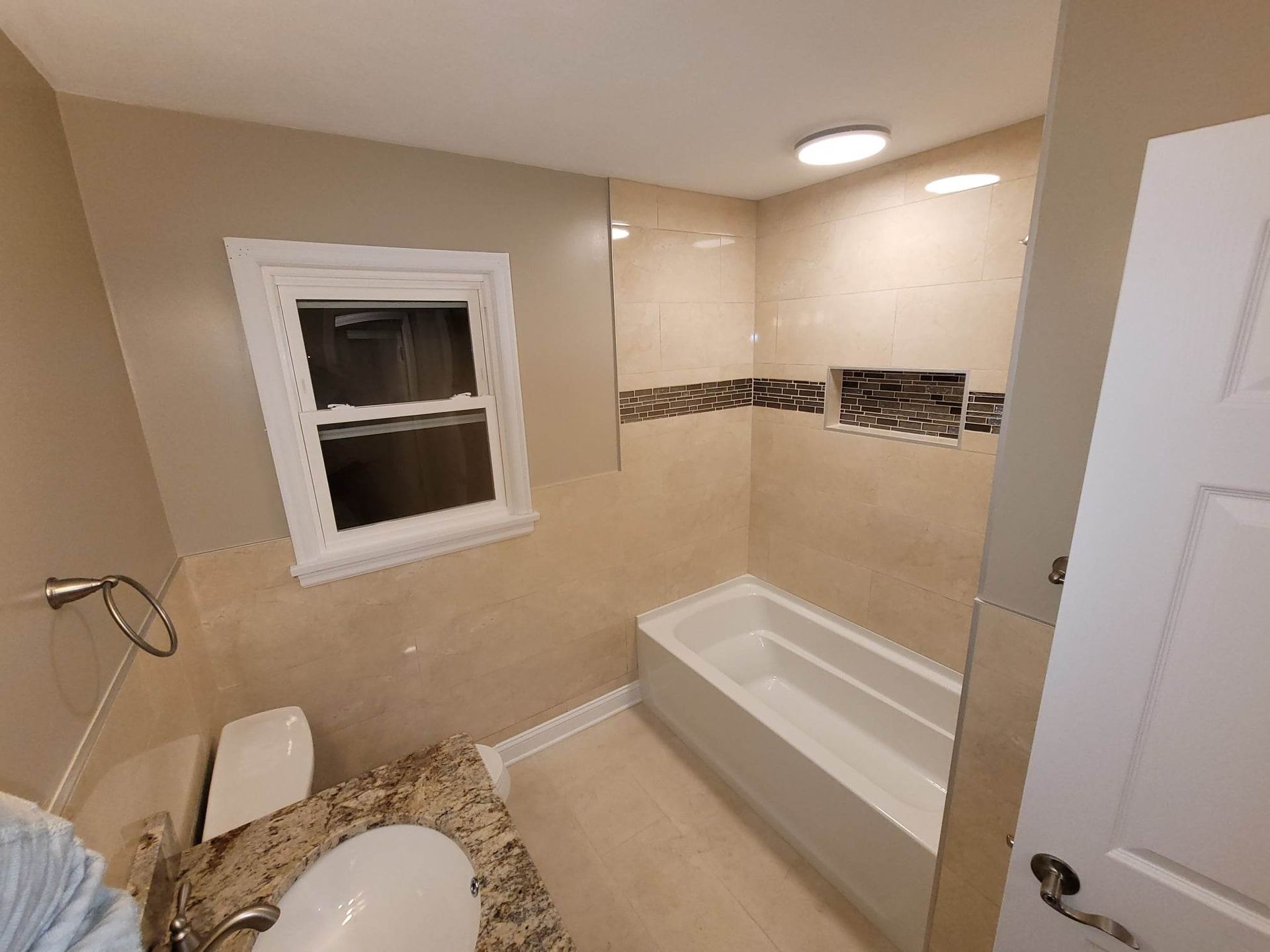 A bathroom with a tub , sink , toilet and window.