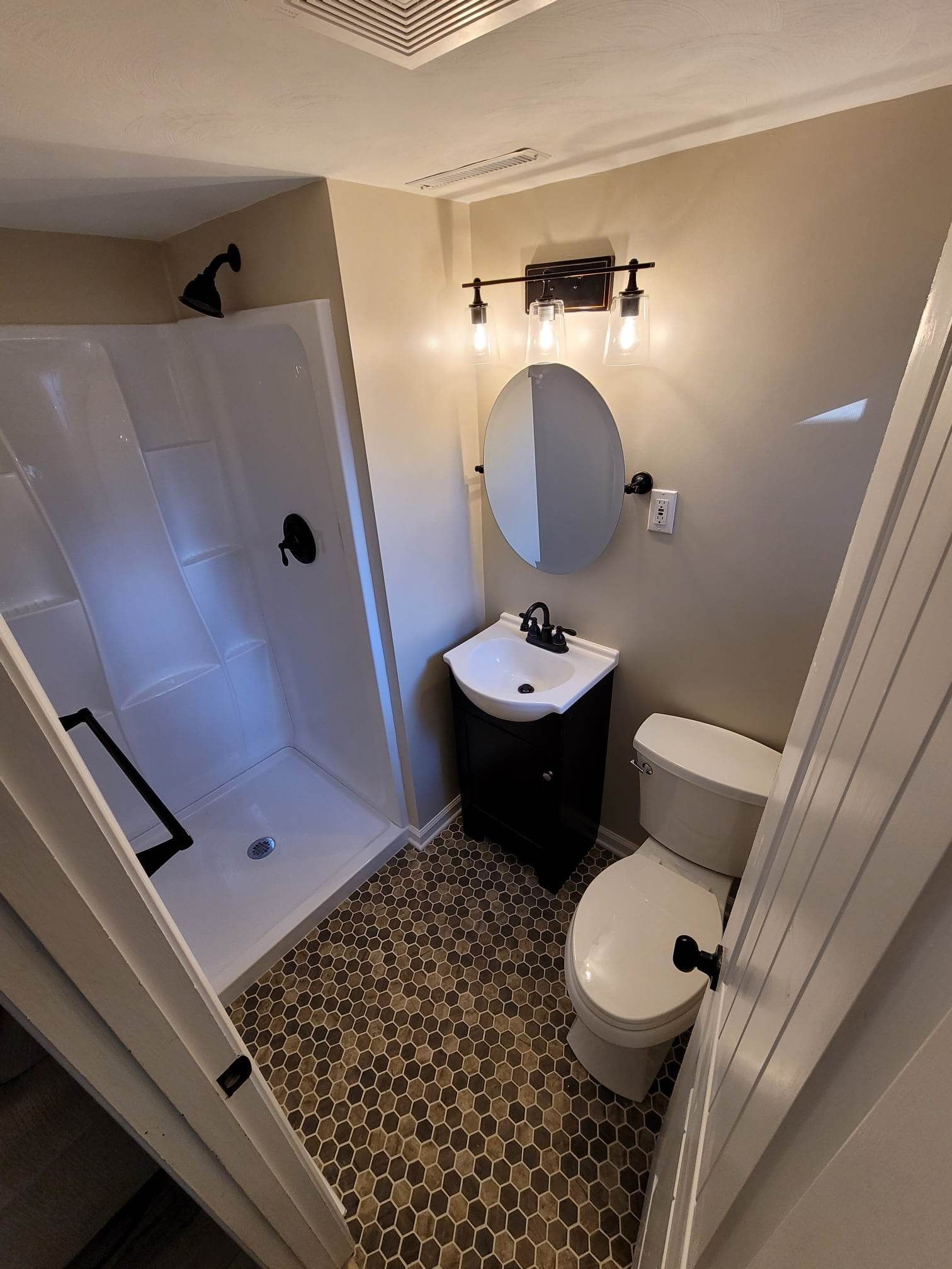 A bathroom with a toilet , sink , shower and mirror.