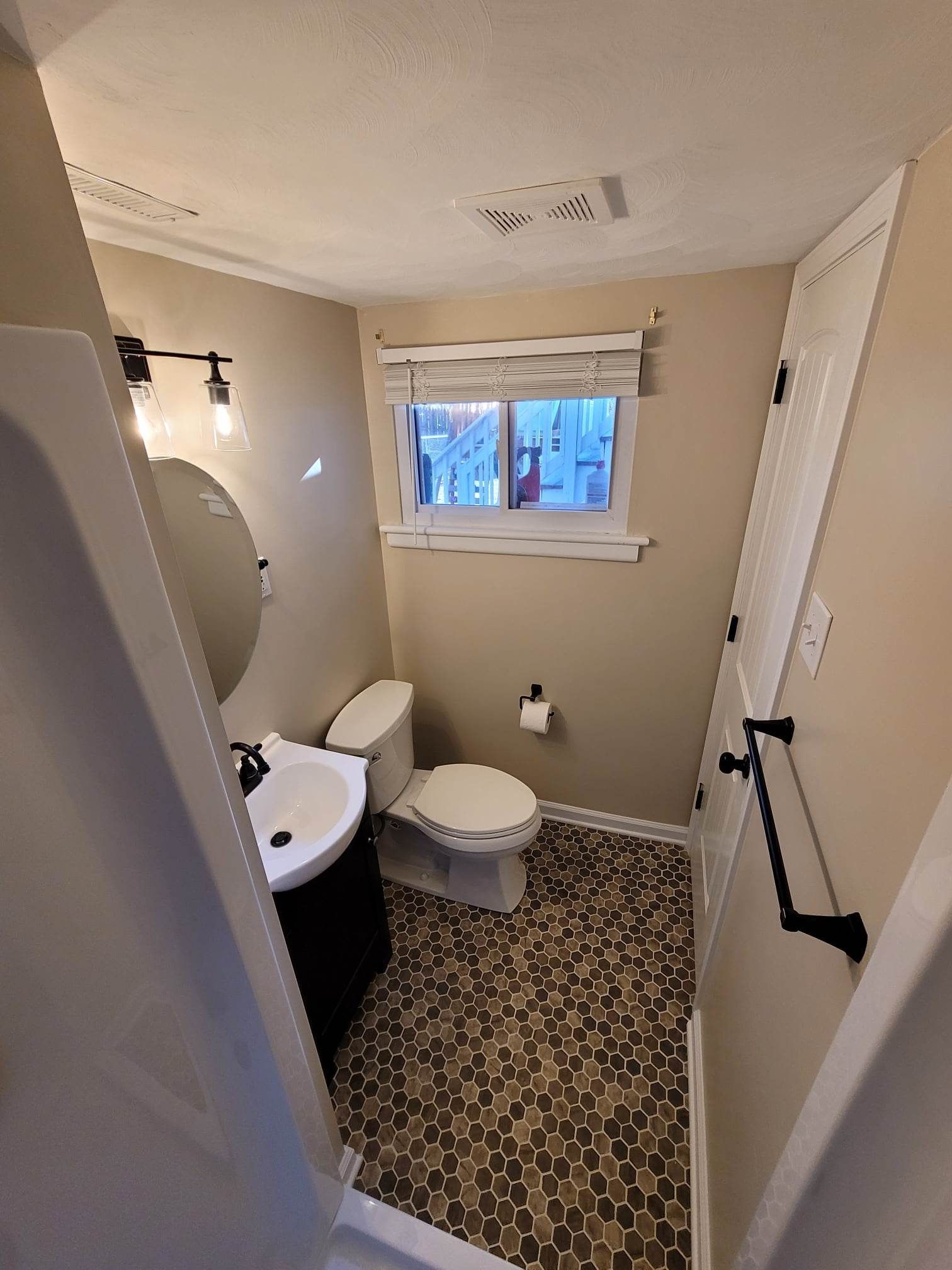 A bathroom with a toilet , sink , mirror and window.