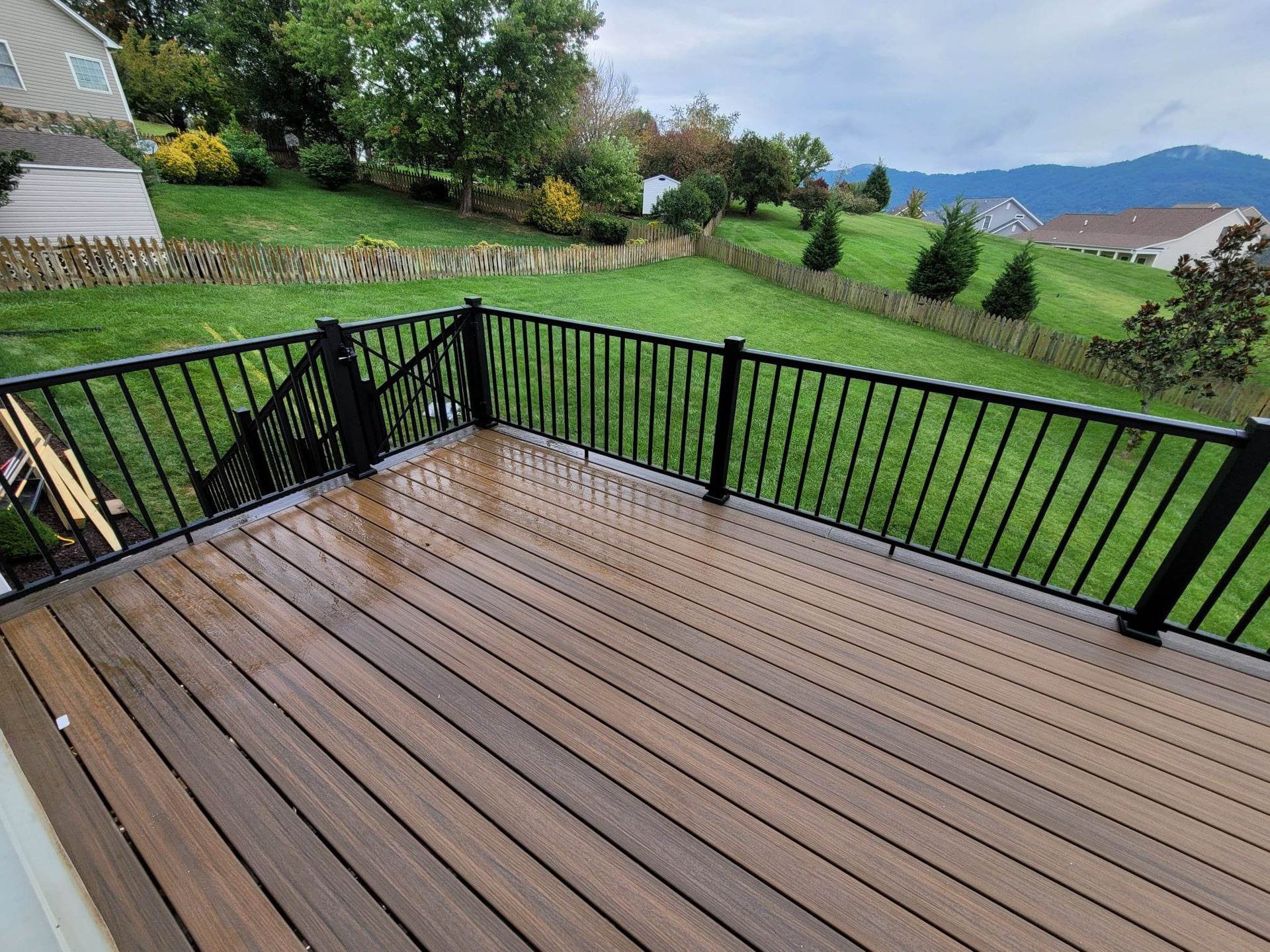 A wooden deck with a black railing and a view of a lush green field.