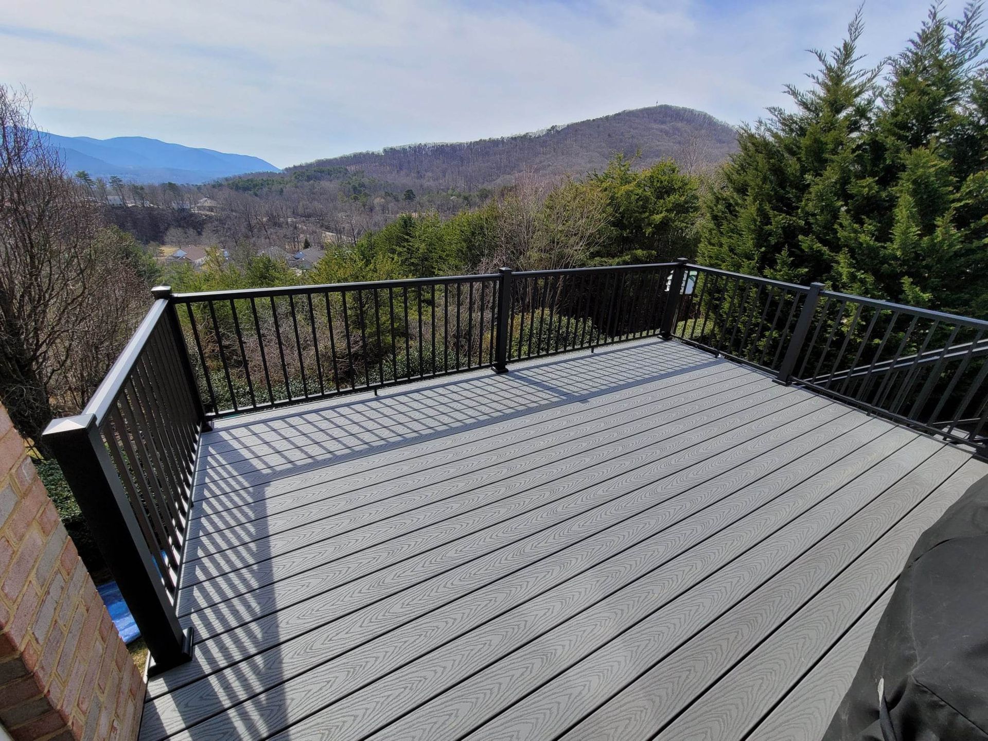 A gray deck with a black railing and mountains in the background.