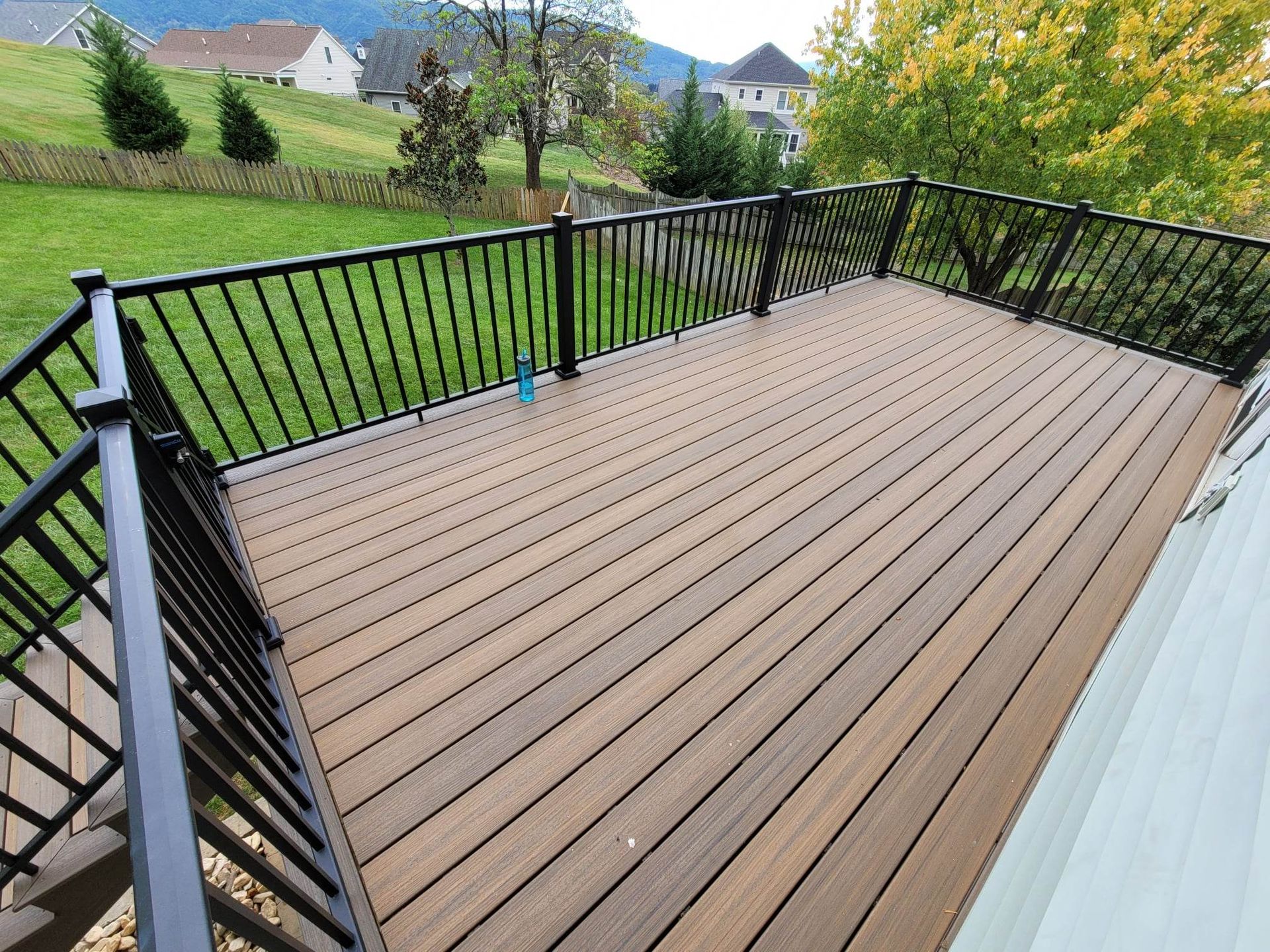 A large deck with a black railing and a view of a lush green field.
